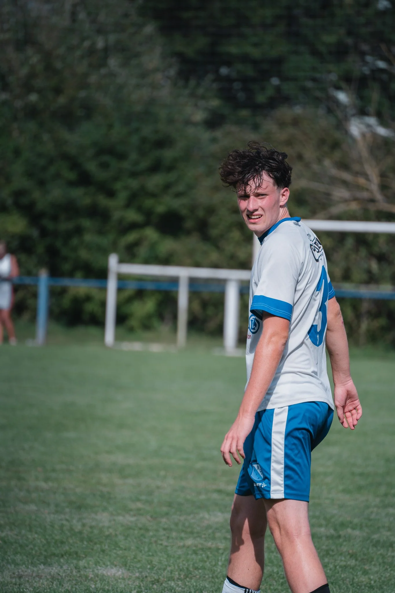 Jeune homme en tenue de football sur un terrain, avec un expression concentrée ou confuse.