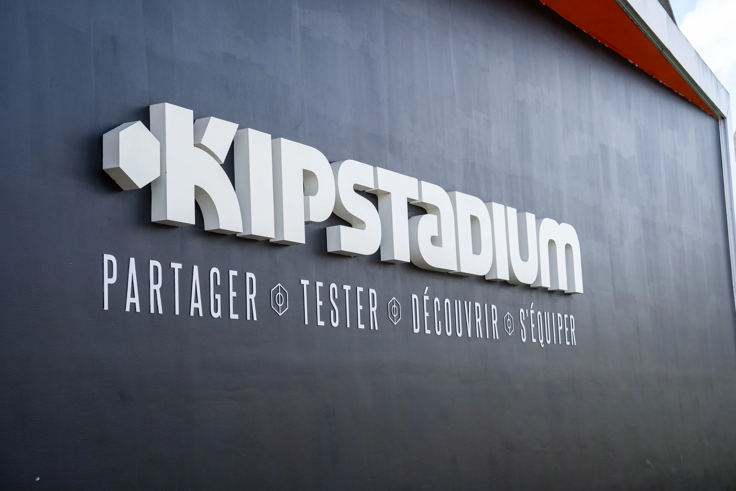 Signalétique du Kipstadium avec le slogan 'Partager, Tester, Découvrir, S'Équiper' sur un mur noir