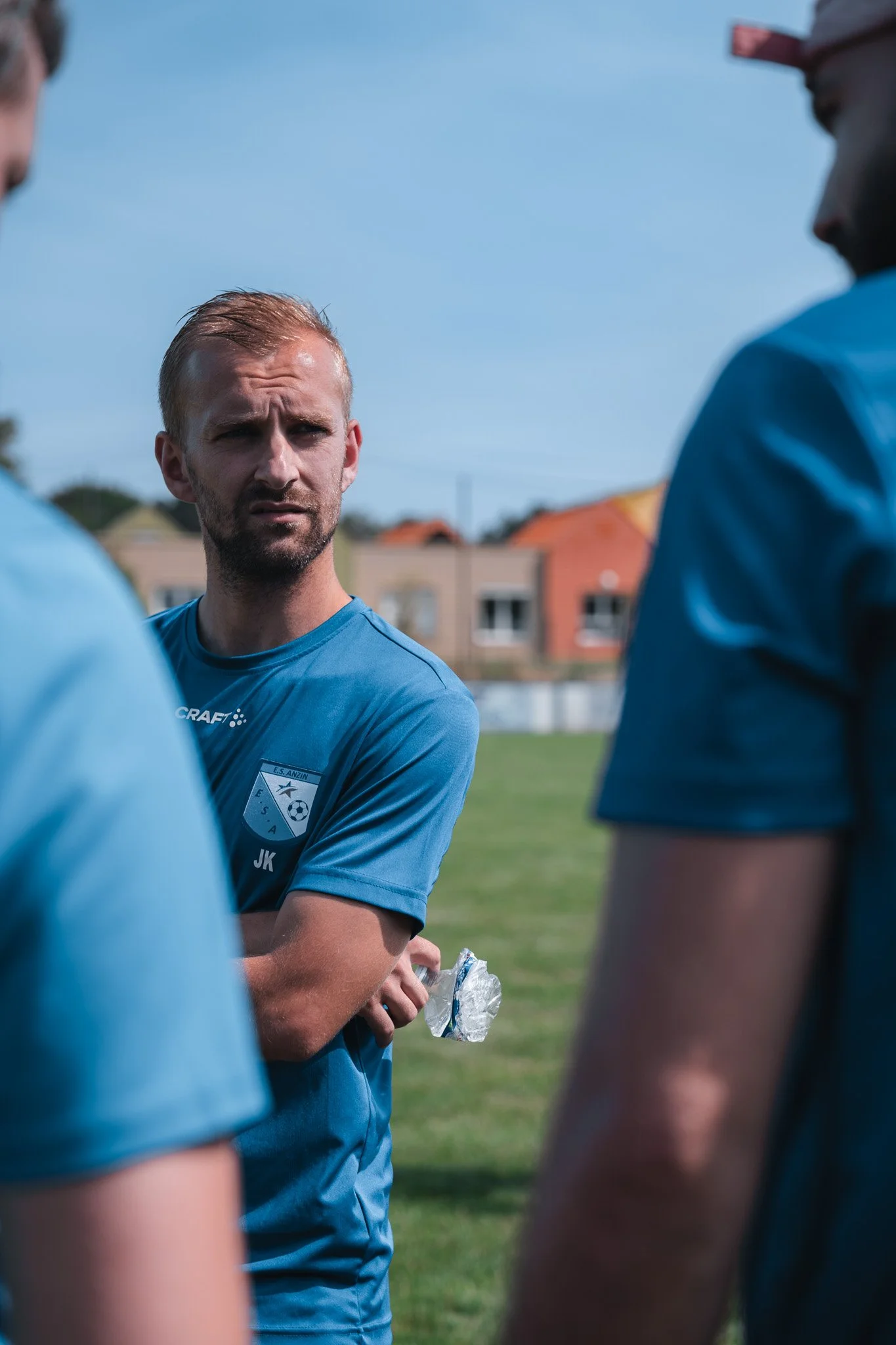 Un entraîneur ou un joueur de football en train de discuter avec ses coéquipiers sur un terrain en plein air, portant un maillot bleu.