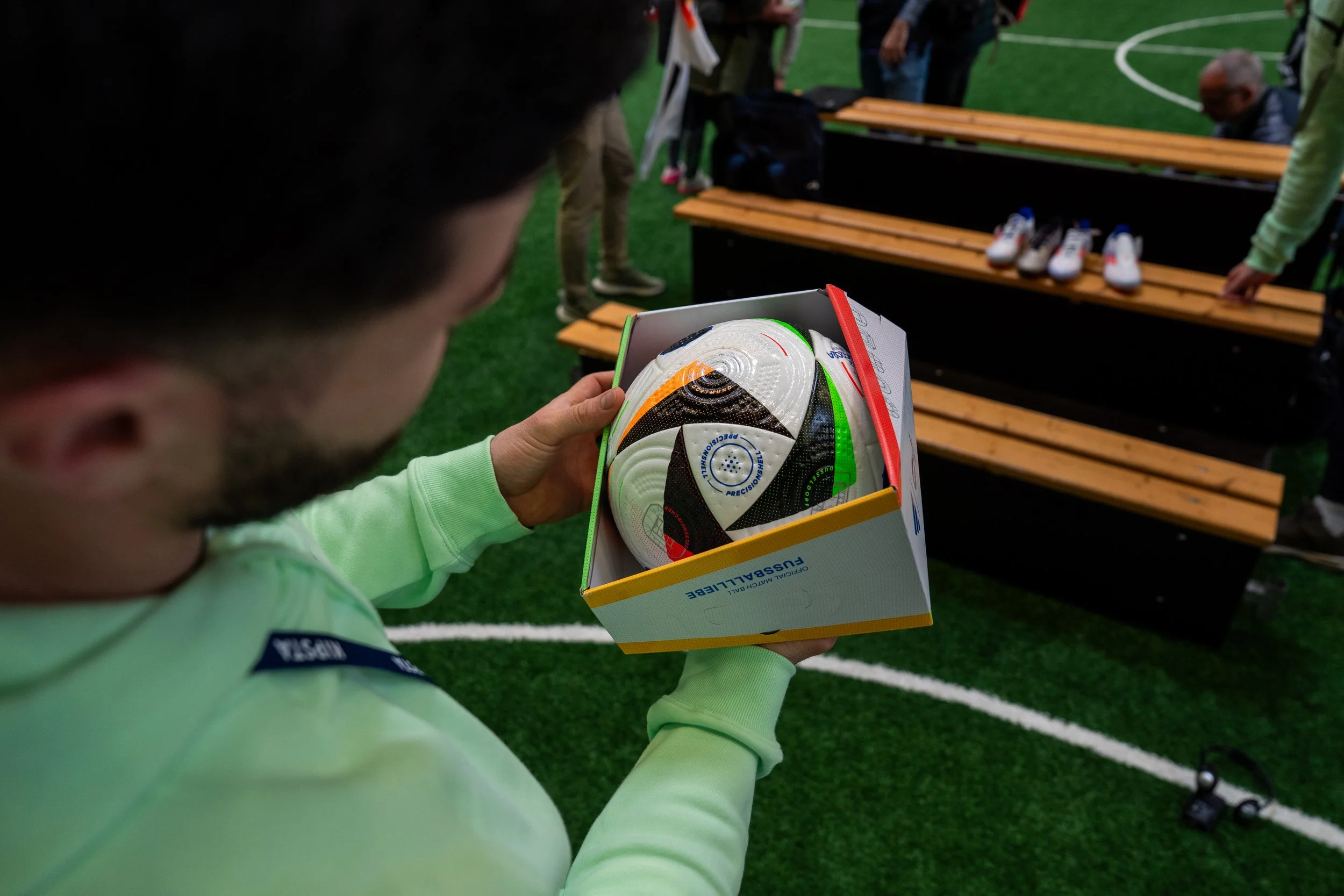 Une personne regarde un ballon de football neuf dans une boîte lors d'un événement sportif en intérieur.