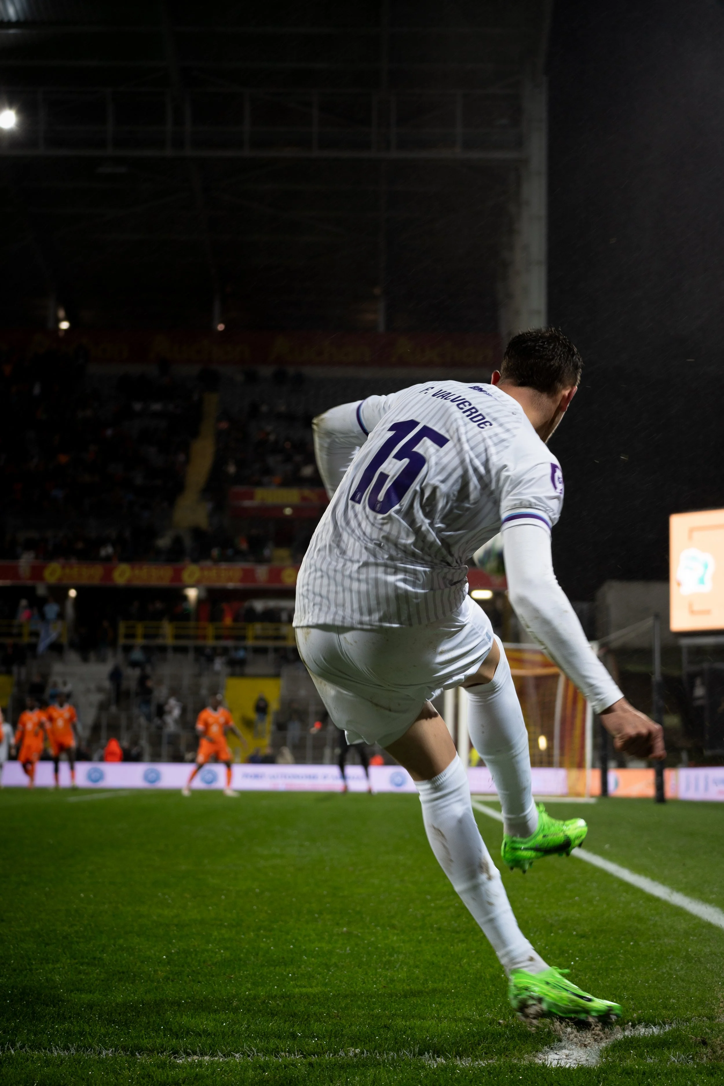 Un joueur de football en train de tirer un coup franc, portant le maillot numéro 15, lors d'un match de nuit sous la pluie dans un stade