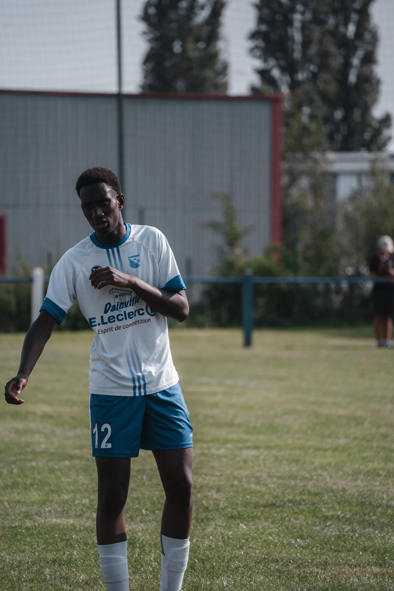 Jeune joueur de football noir portant un maillot blanc et bleu, numéro 12, sur un terrain de sport en pleine action.