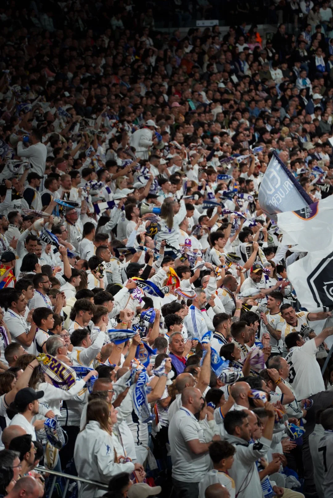 Grande foule de supporters de football portant des maillots blancs et brandissant des drapeaux, dans un stade