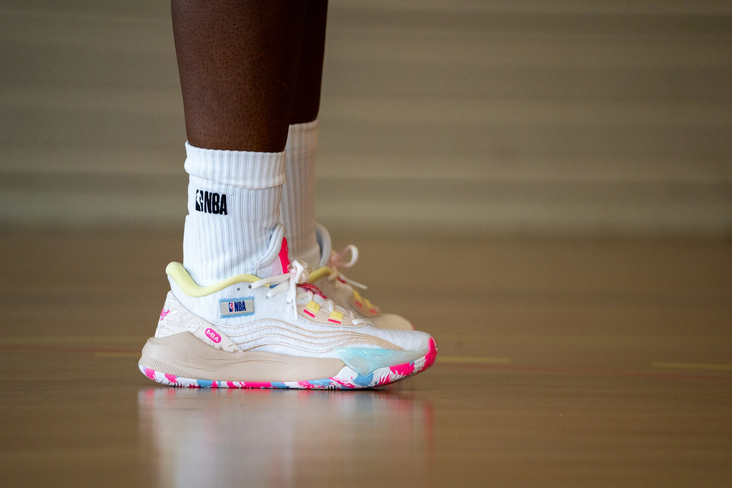 Chaussures de basket-ball blanches avec des détails roses, jaunes et bleus portant le logo NBA et le nom 'MIA'.