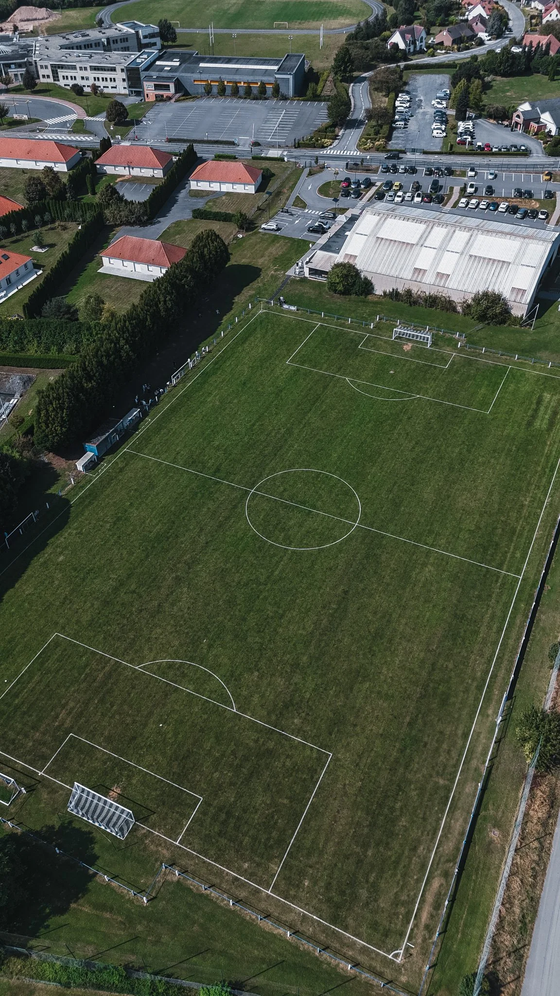 Terrain de football en plein air entouré de bâtiments, avec des lignes blanches délimitant le terrain, une porte de but, et des lignes de touche.