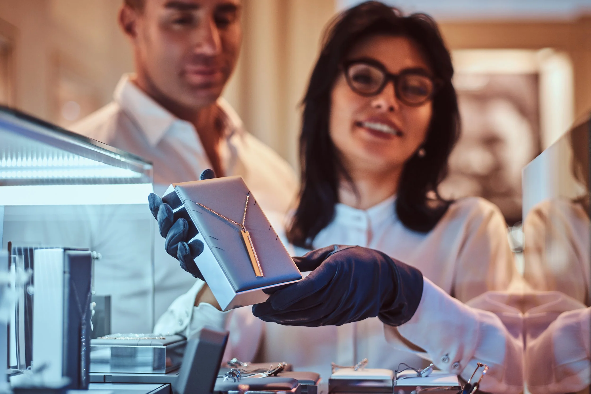 A woman with glasses and dark hair showing a necklace to a man at a jewelry store.