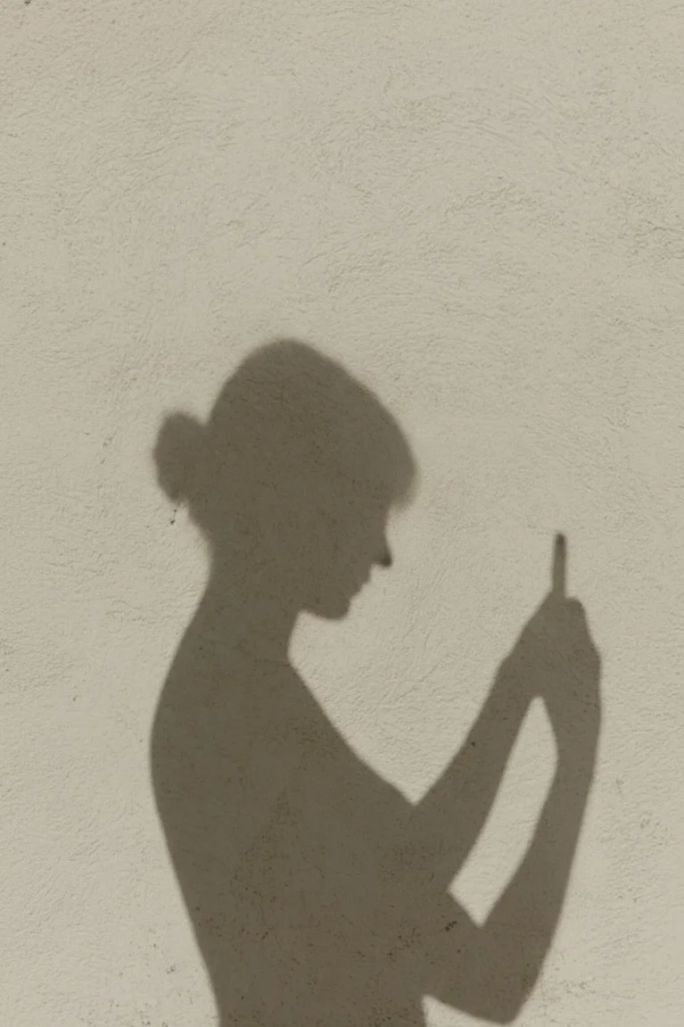 Shadow of a woman holding a lipstick against a beige textured wall.
