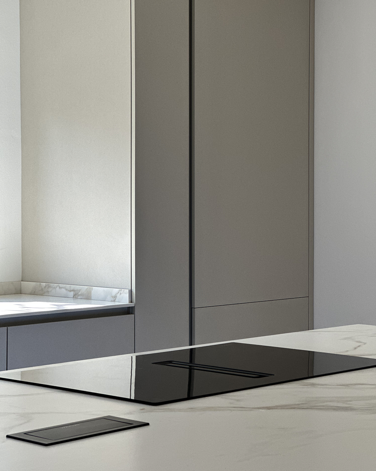 Modern kitchen with gray cabinets, marble countertop, and black stovetop.