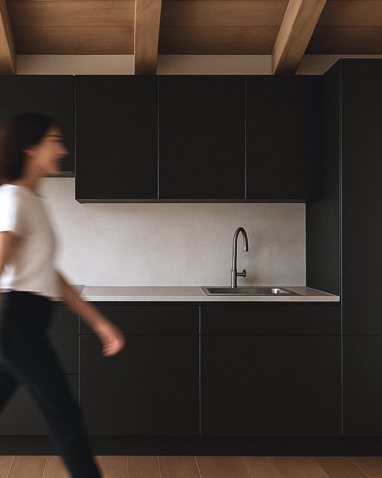 A woman walking past a minimalist kitchen with black cabinets, a stainless steel sink, and a wooden ceiling.
