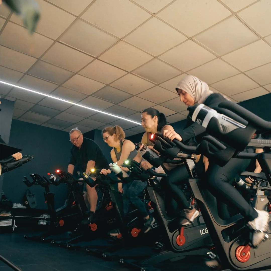 People participating in a group indoor cycling class on stationary bikes in a fitness studio.