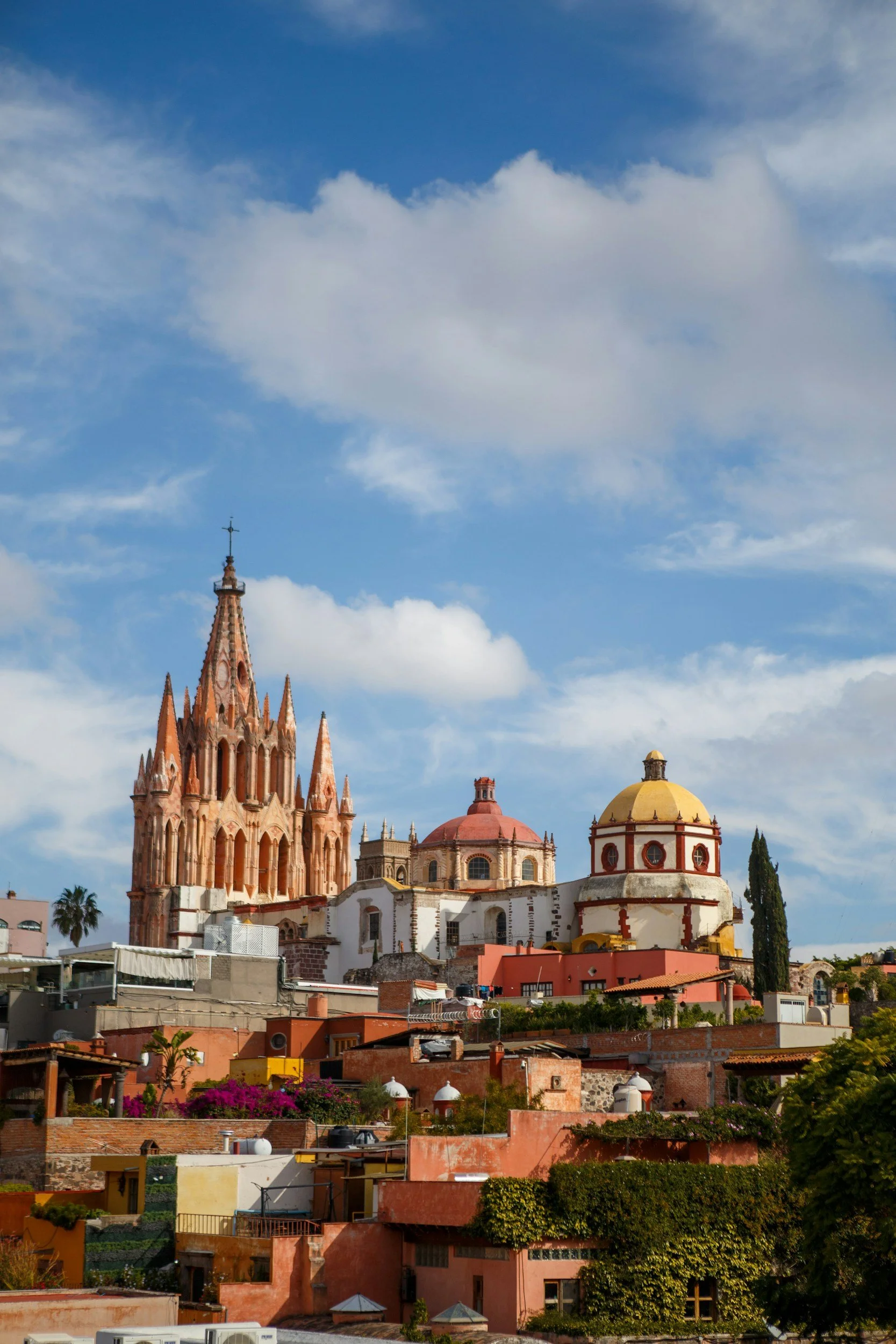 Colorful buildings and churches on a hillside, with a blue sky and clouds overhead.