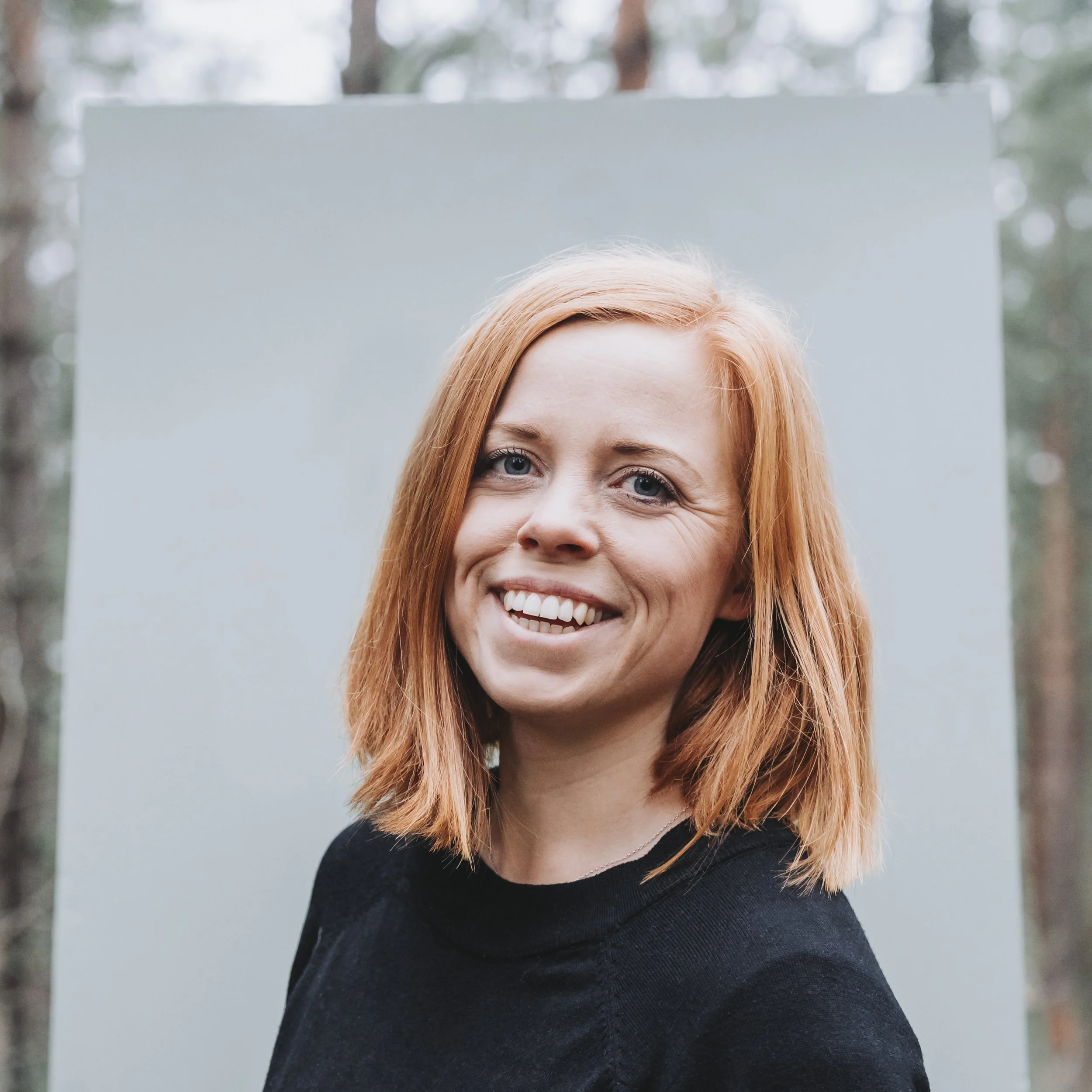 Ung kvinna med rödhårigt hår och blå ögon skrattar utomhus. Johanna Egemar, företagsfotograf.