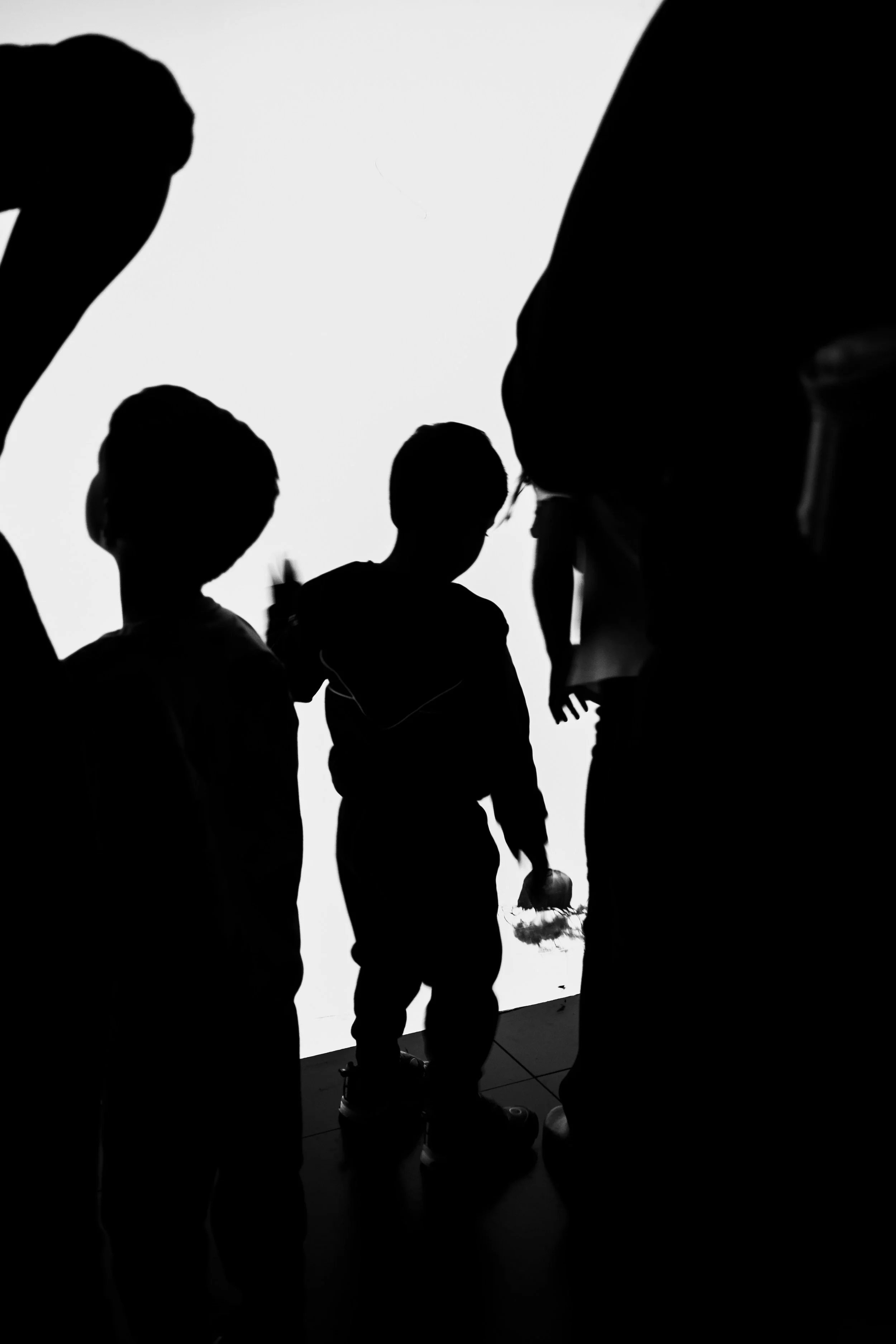 Silhouettes of children and adults standing in front of a bright, white background, possibly in an indoor exhibit or museum.