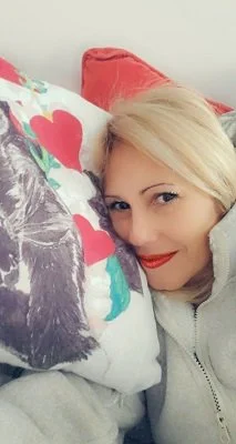 Anissa Mendez resting her head on a colorful pillow featuring hearts, smiling at the camera in a cozy setting.