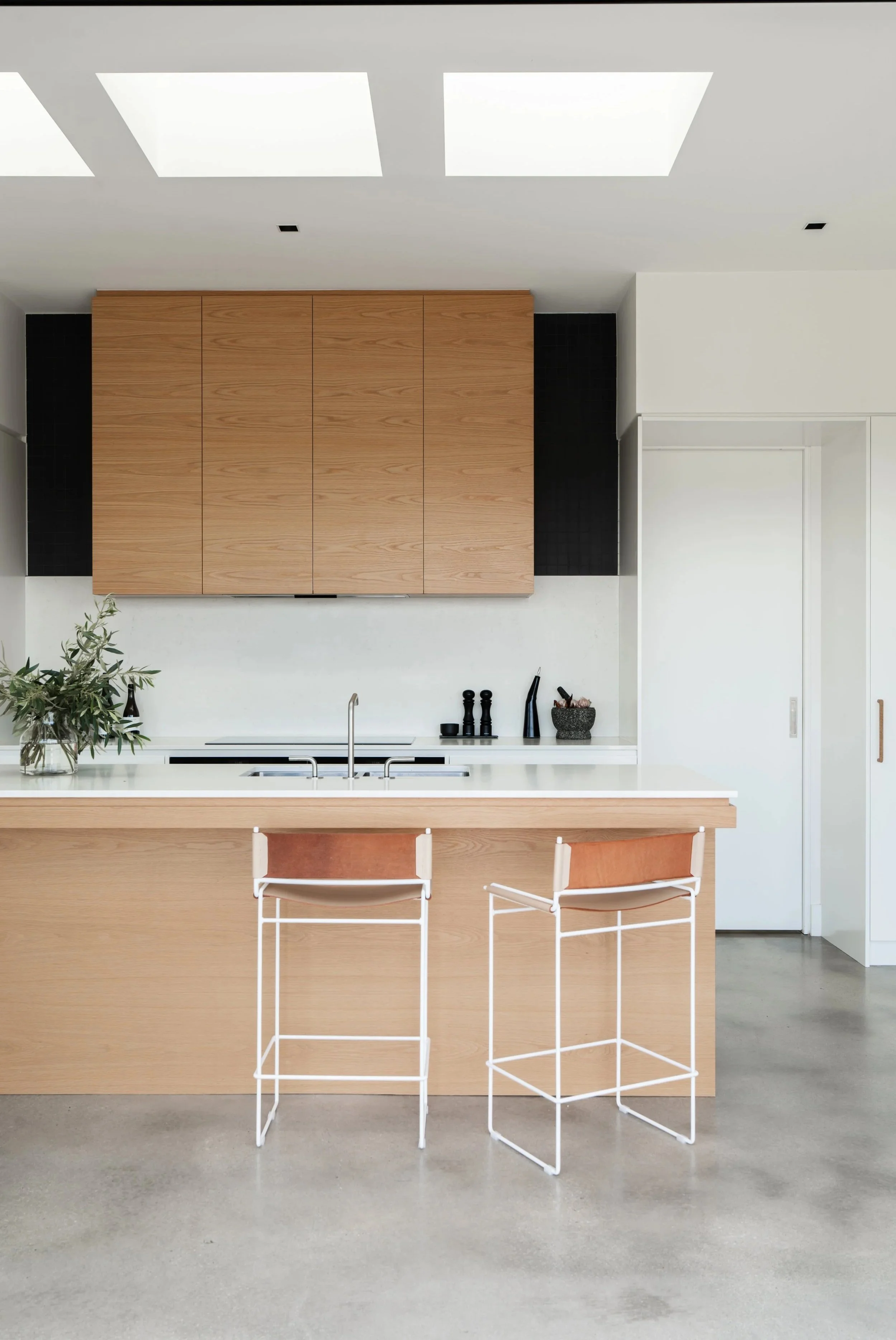 Interior kitchen with 3 large skylights centred above a light oak island bench with breakfast stools and decorated kitchen