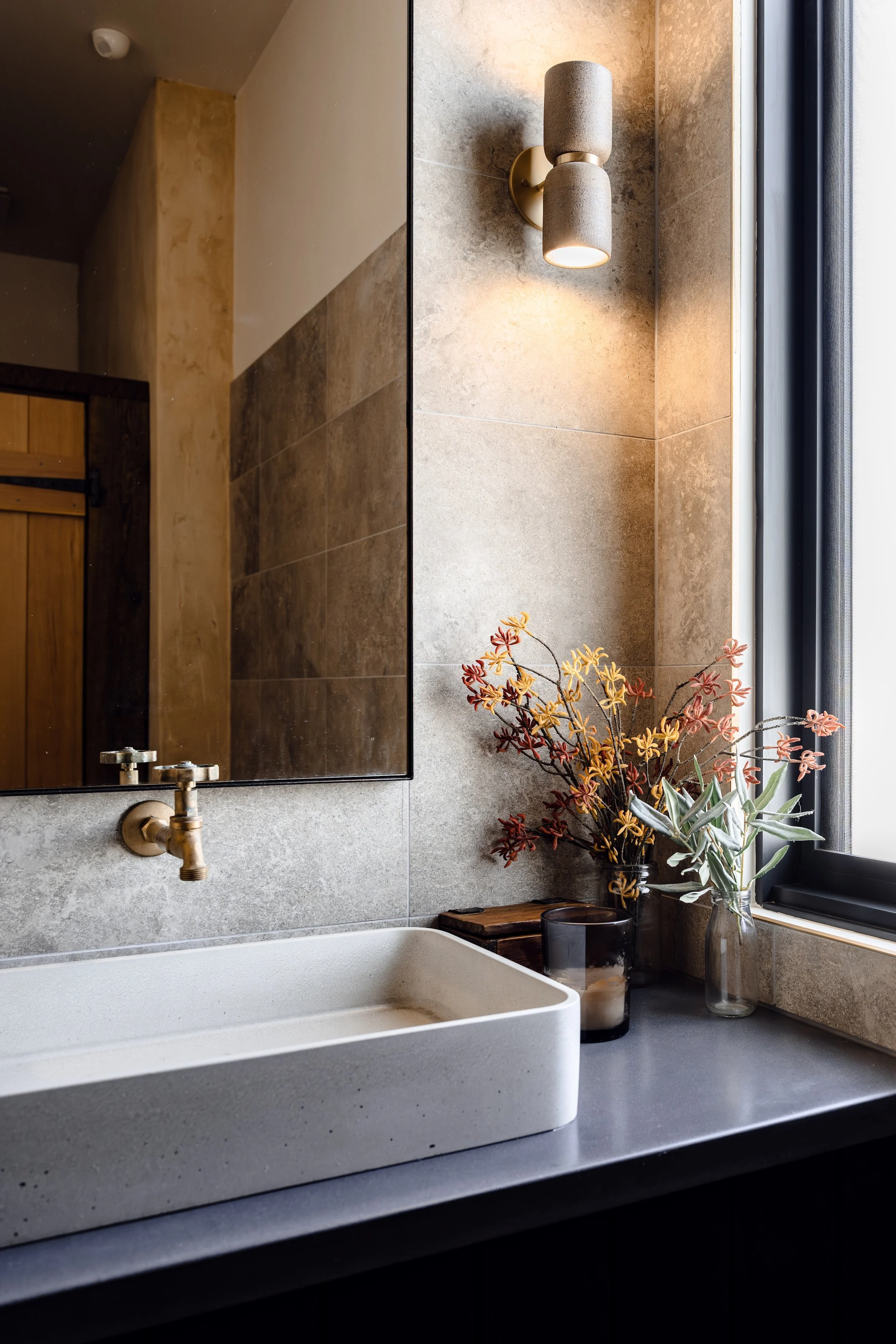 Concrete basin, brass tapware and native flowers against rustic textured render, bathroom in 100-year-old stone barn restoration