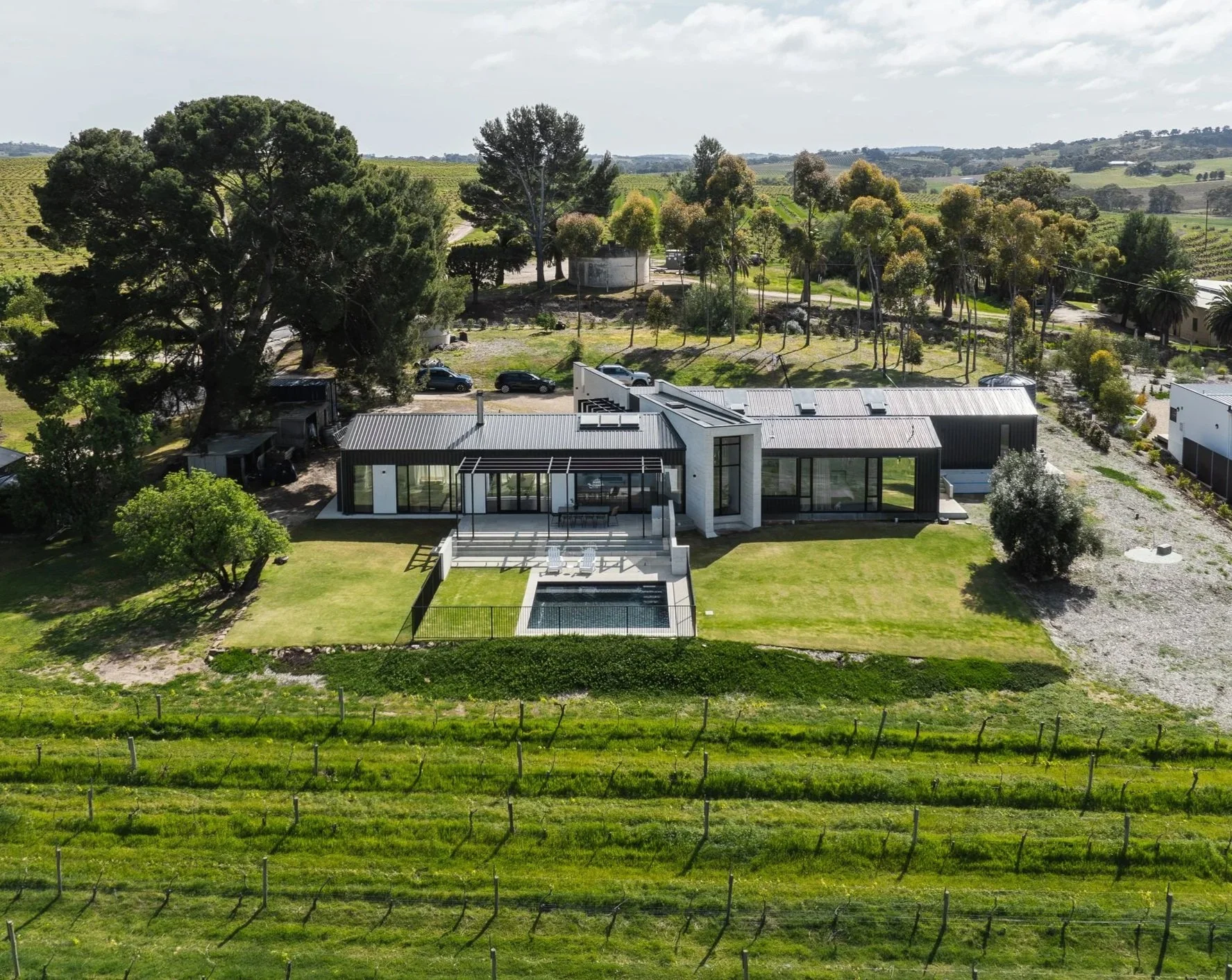 Drone image of an architectural new build with a pool and large outdoor area,  located in the Barossa Valley, surrounded by greenery overlooking vineyards