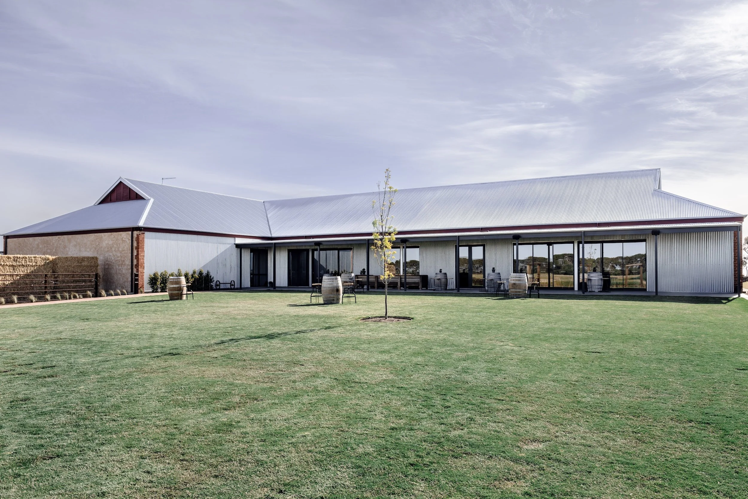 Heritage barn restoration by Bishop Building, surrounded by a large manicured lawn, hay bales and barrel seating