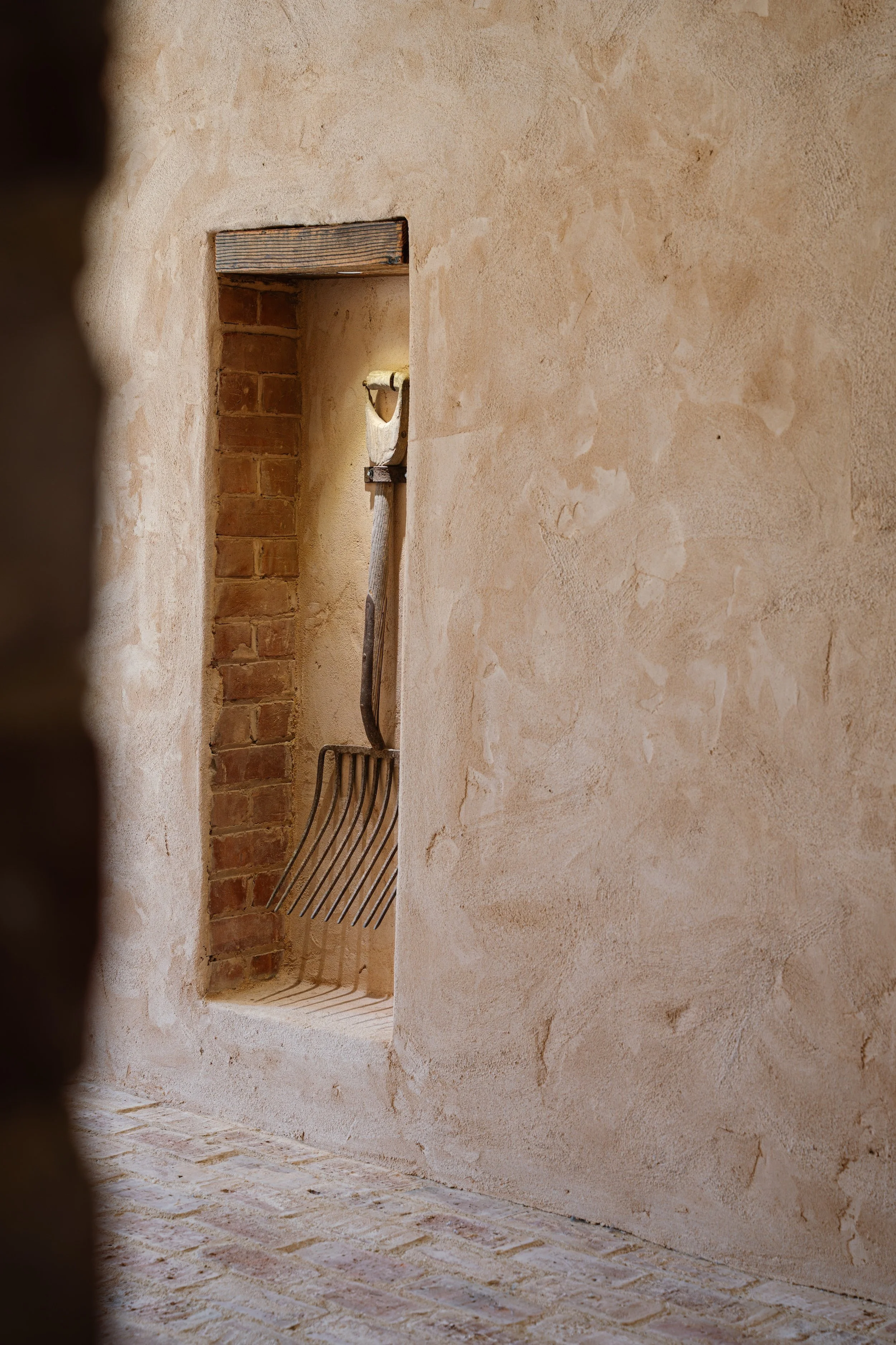 Vintage pitchfork displayed in a lit brick alcove with exposed timber lintel, heritage detail at Stables of Halcyon