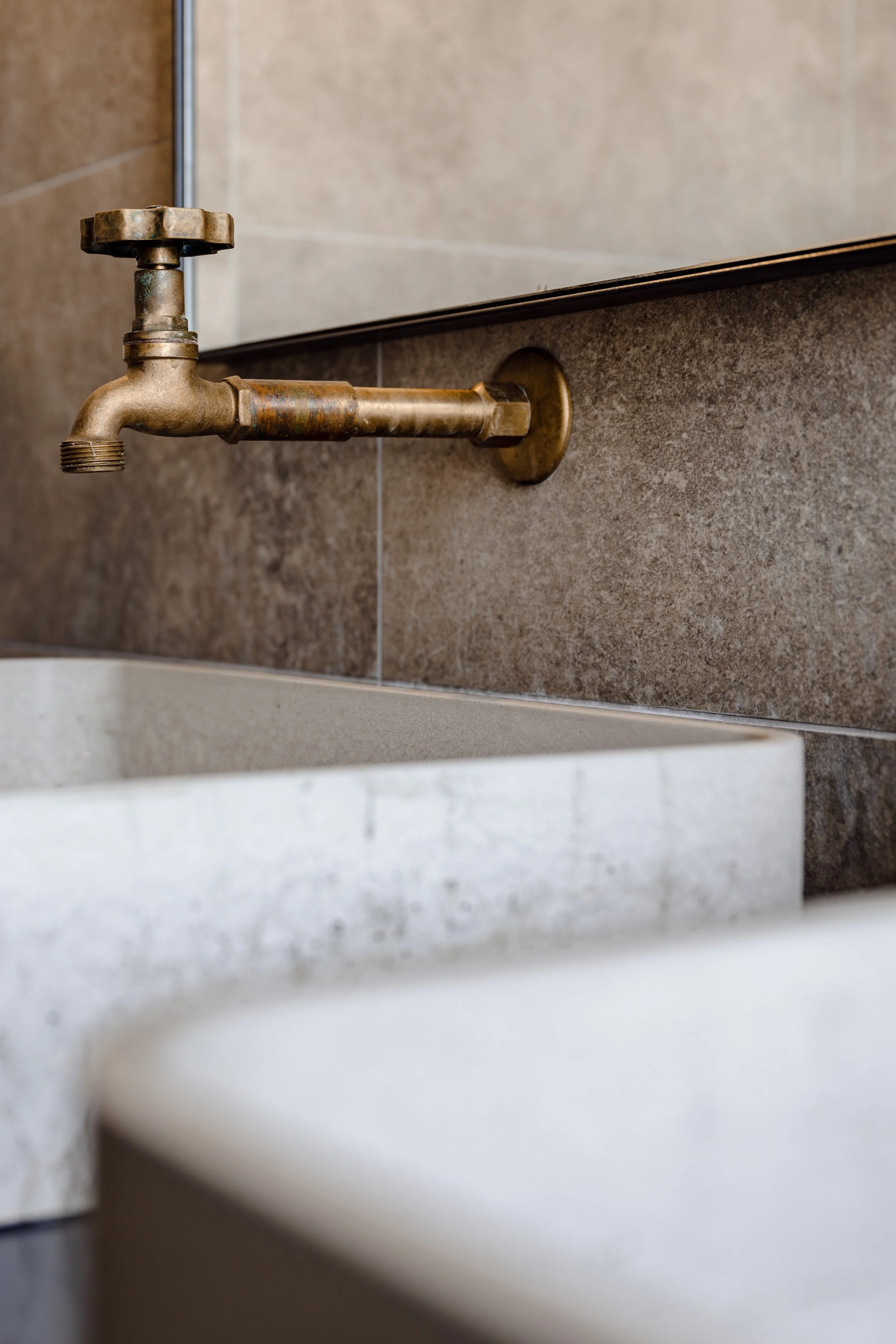 Wall-mounted rustic brass tap over concrete basin, bathroom detail at Stables of Halcyon