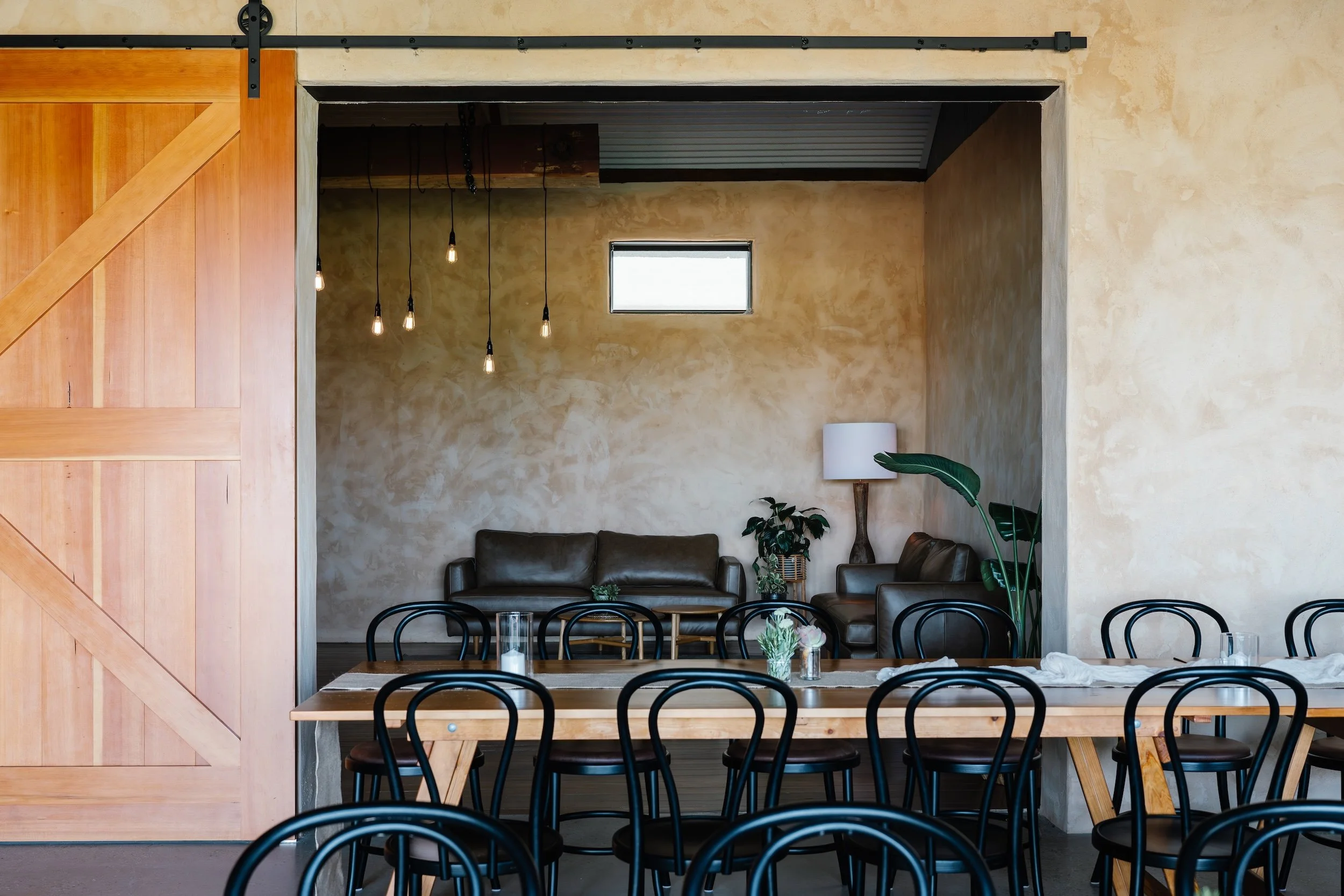 View through open timber barn door to leather lounges, bentwood chairs and festoon lighting inside event space