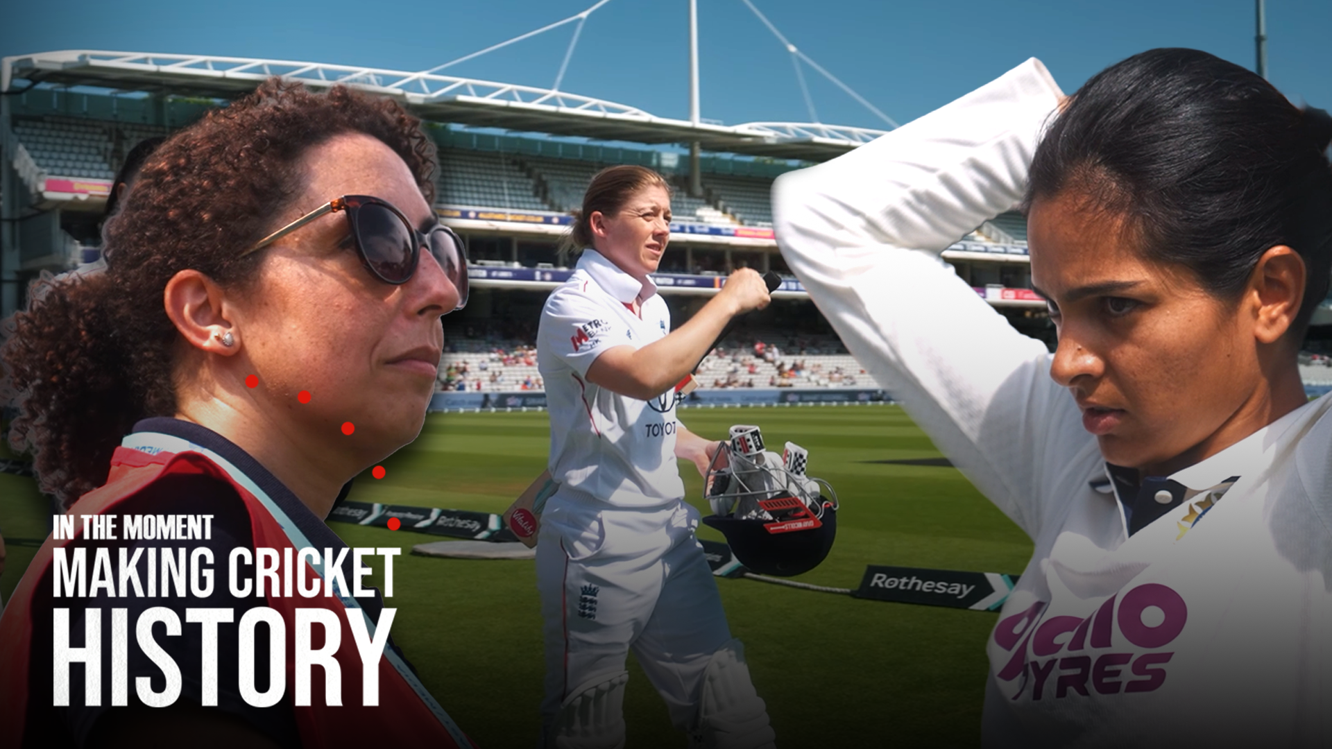 A cricket stadium with three women in cricket uniforms, two of them are facing each other with one fixing her hair and the third one is speaking into a microphone. The stadium stands are visible in the background under a clear blue sky.