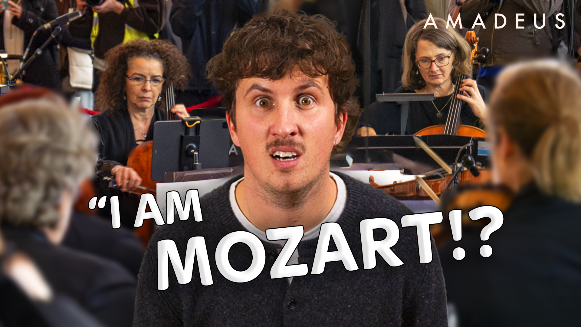 Man with surprised expression in front of an orchestra, with visible musicians playing cellos, and the text "I AM MOZART!?" superimposed on the image.