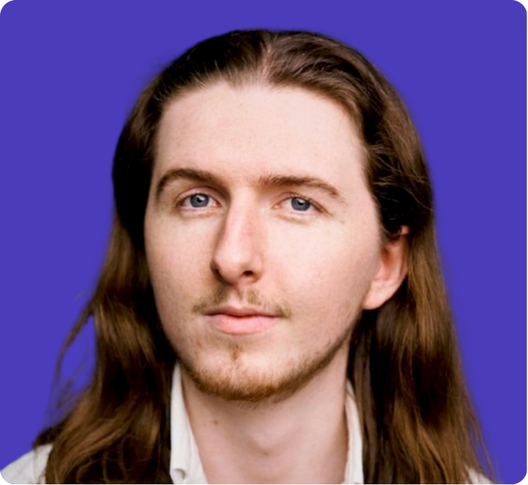 Portrait of a young man with long brown hair and blue eyes against a blue background.