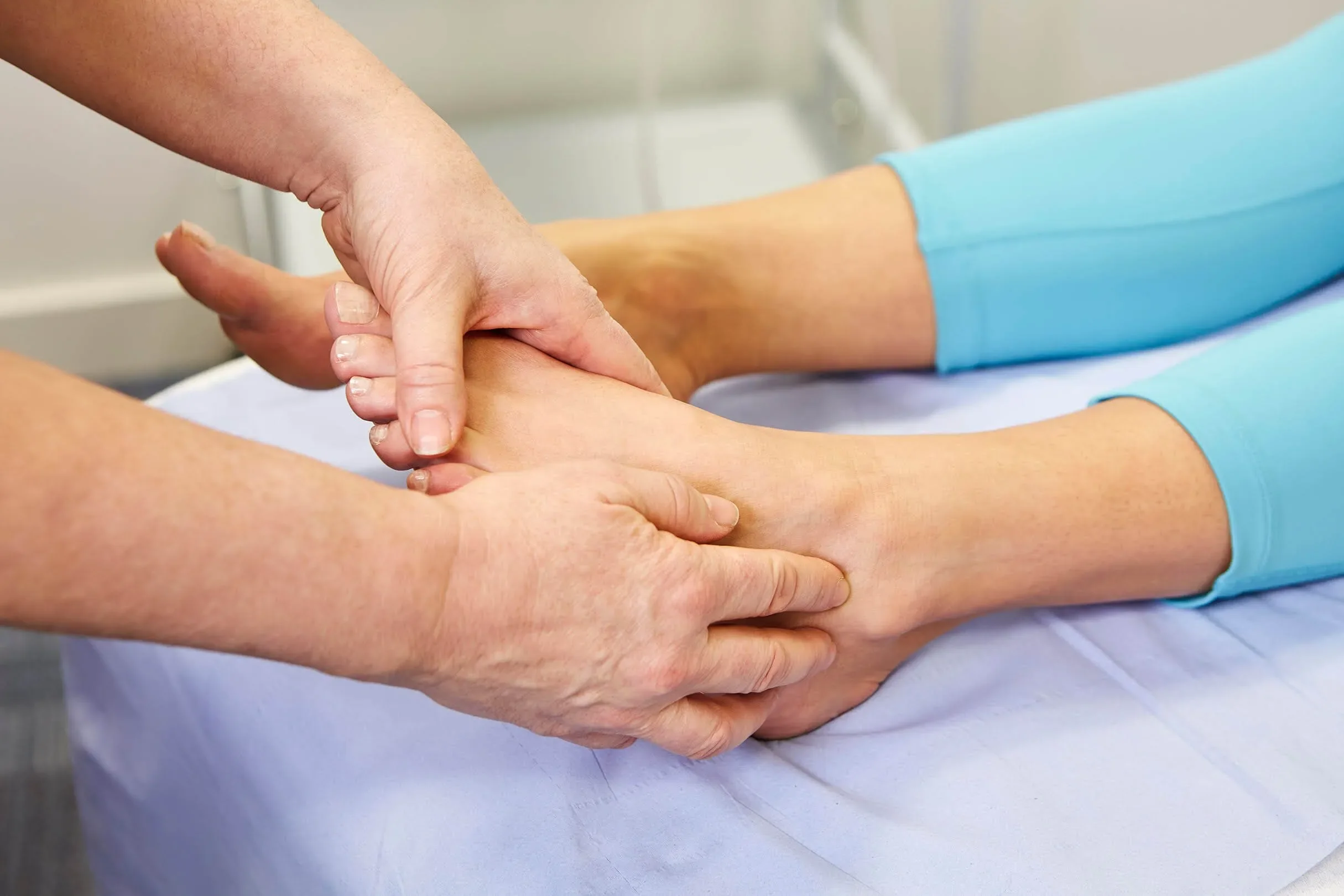 Close-up of a physical therapist or healthcare provider hand holding a patient's arm, performing a physical therapy or medical examination in a clinical setting.