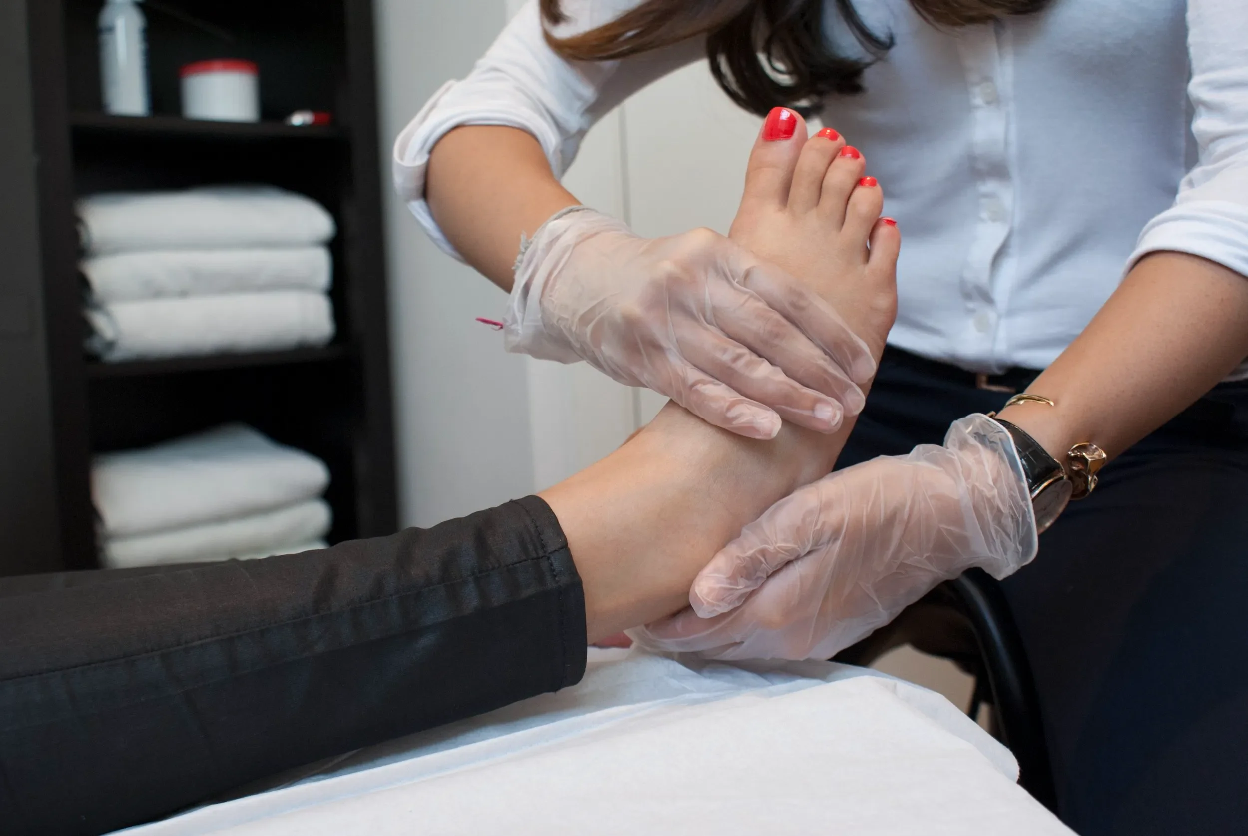 A healthcare professional wearing gloves performing a procedure on a patient's hand in a clinical setting.