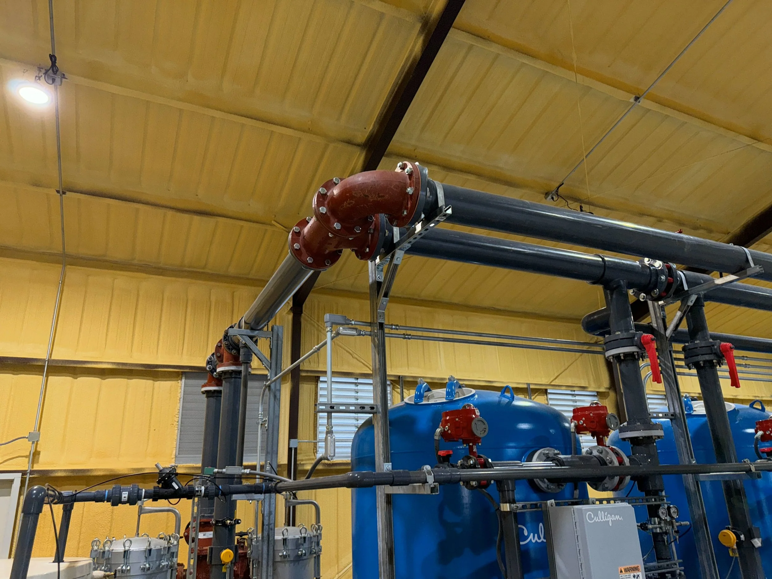 Industrial water filtration system with pipes and blue tanks in a facility.