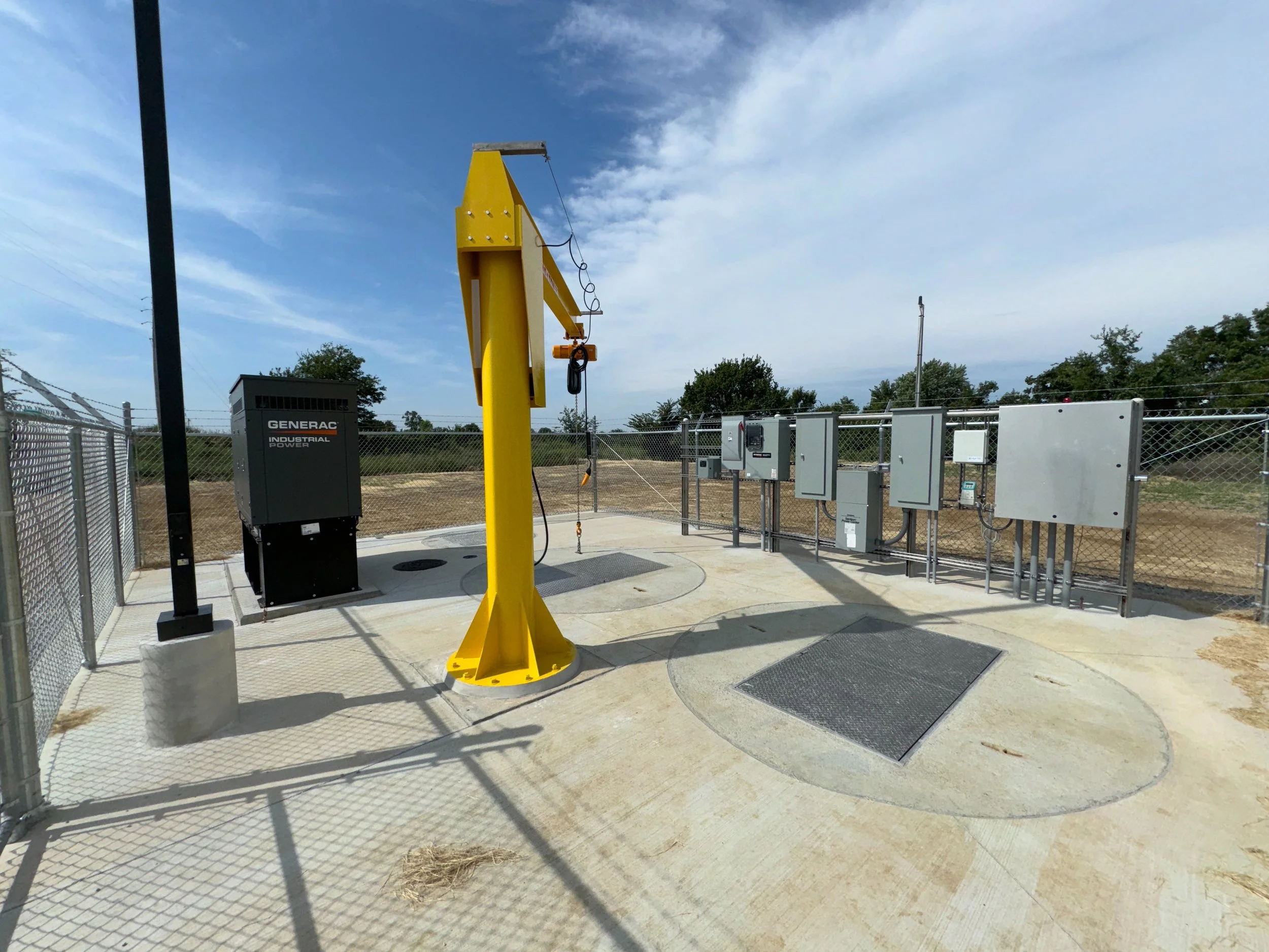 Industrial equipment setup with a yellow crane, Generac industrial power cabinet, electrical panels, and a fenced area outdoors.