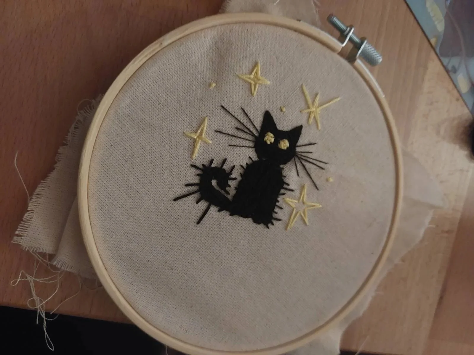 Embroidery hoop with a black stitched cat and four yellow embroidered stars on fabric.