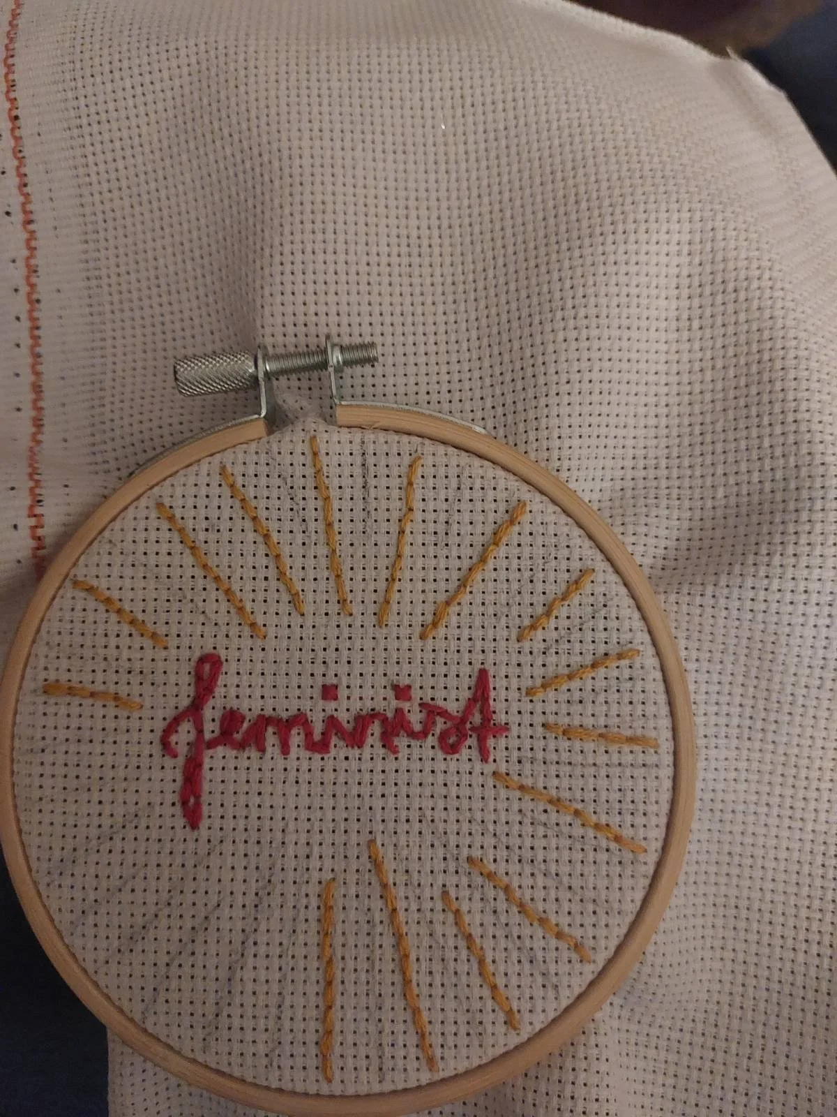 Embroidery hoop with the word "journée" stitched in pink thread, surrounded by yellow rays on fabric.
