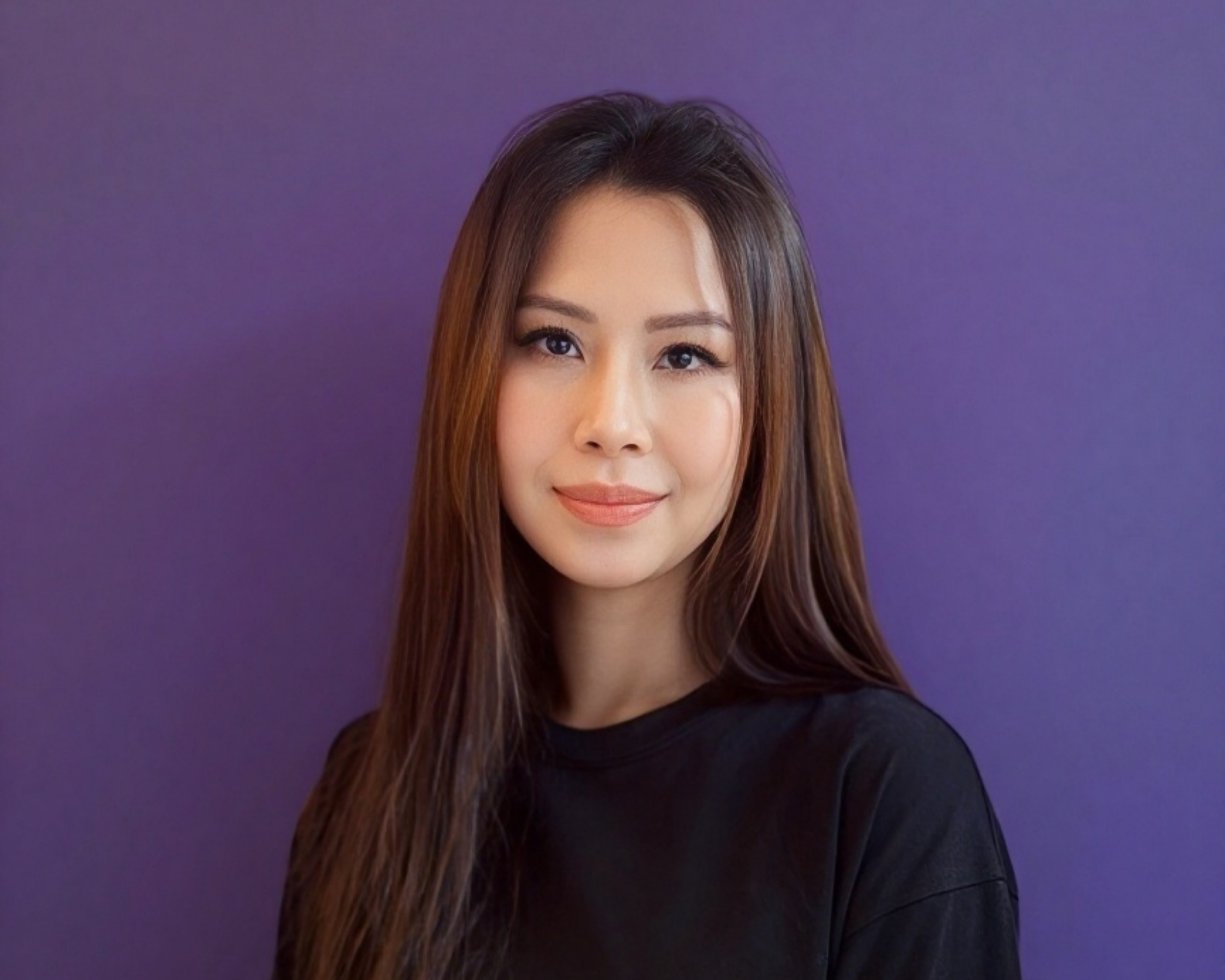 Portrait of a smiling woman with long brown hair wearing a black shirt against a purple background