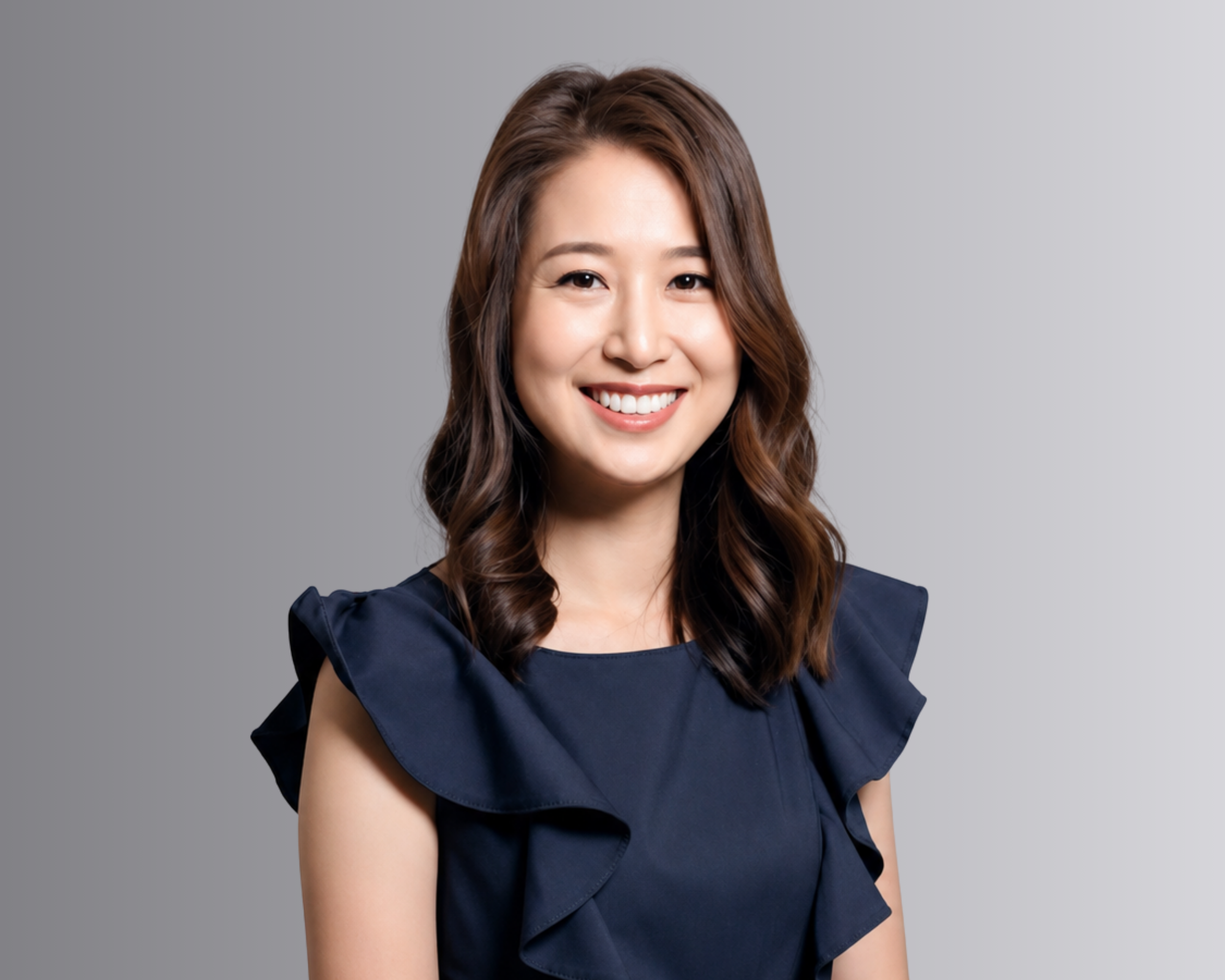 Smiling woman with long brown hair wearing a navy blue ruffled blouse against a gray background
