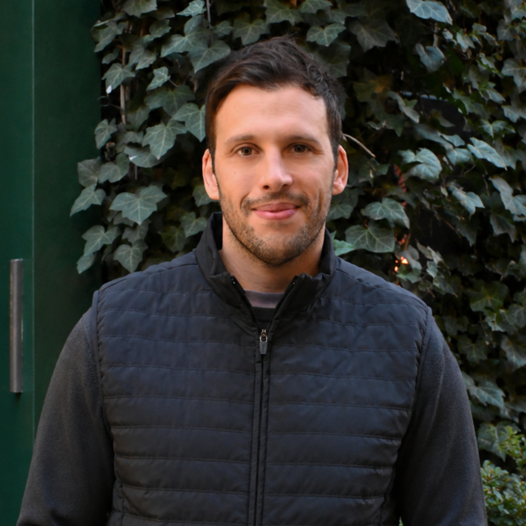 Portrait of a man wearing a black quilted vest in front of an ivy-covered wall