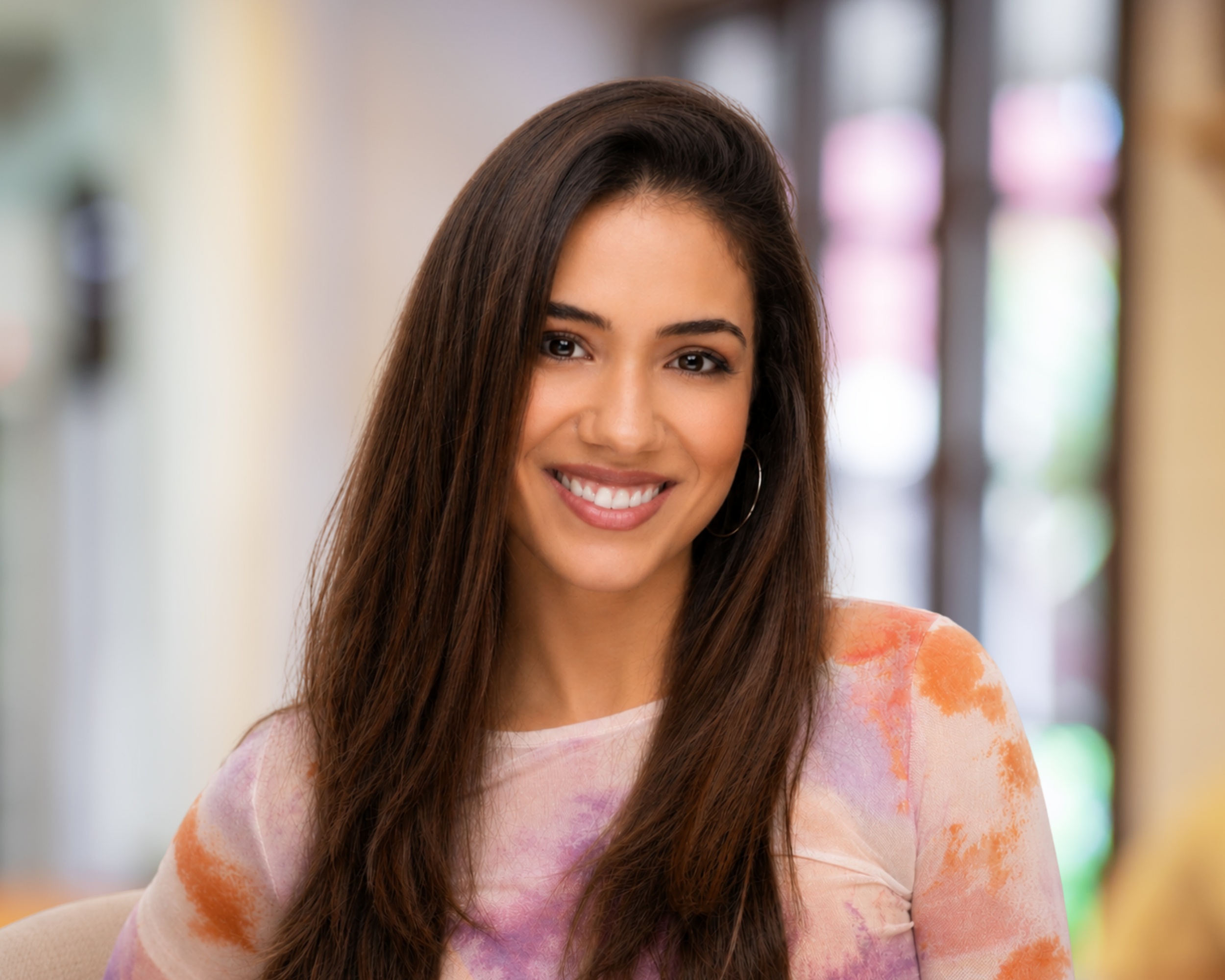 Smiling woman with long brown hair wearing a colorful pink and orange shirt