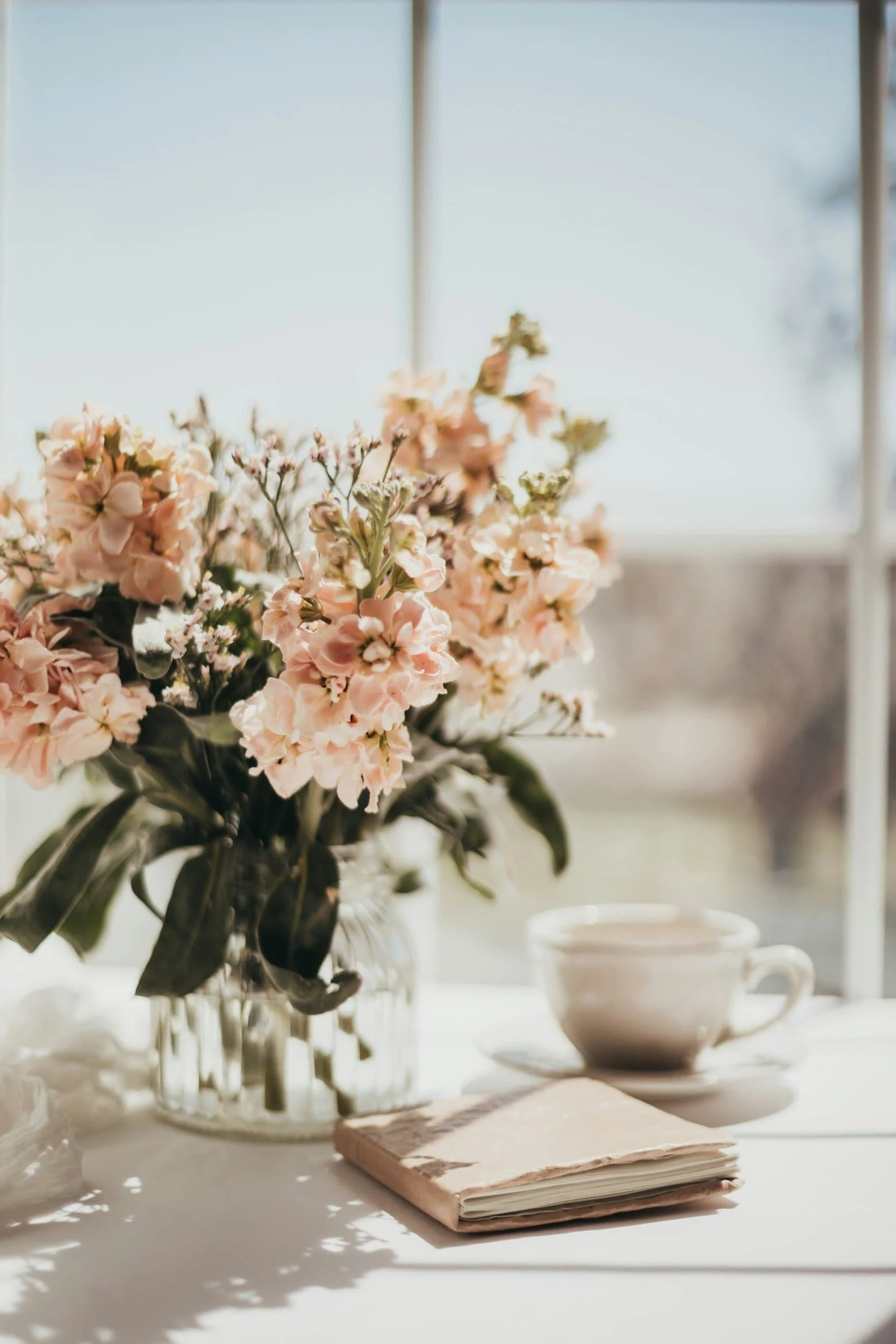 Glass vase with pink flowers, a brown paper notebook and teacup therapy for women in Medicine Hat Alberta