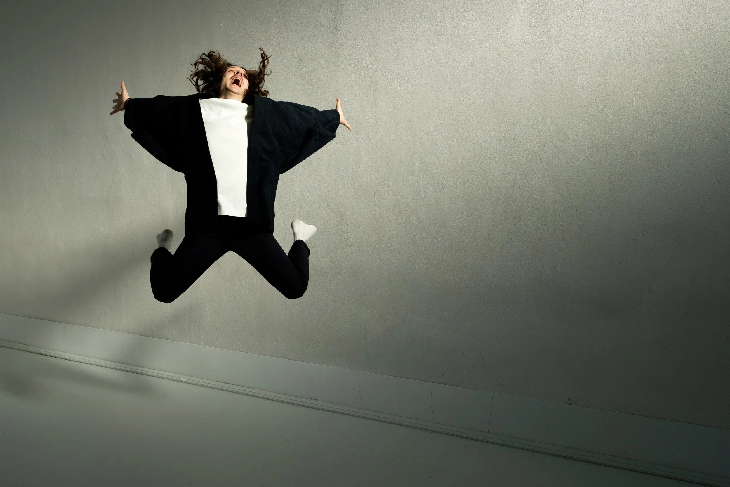 Person jumping and expressing joy or excitement, with hair flying, against a plain background.