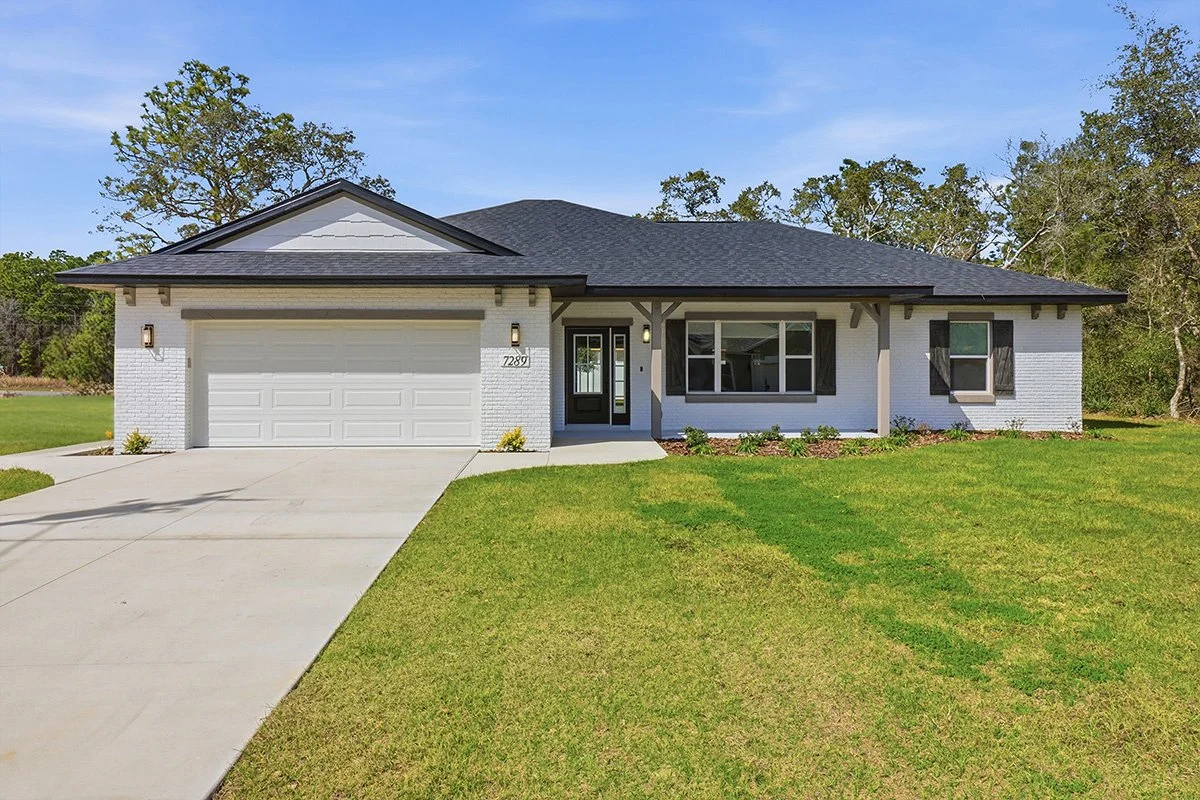 Front exterior of a ranch-style home with white brick siding, a dark gray roof, and a covered front porch with wooden support beams.