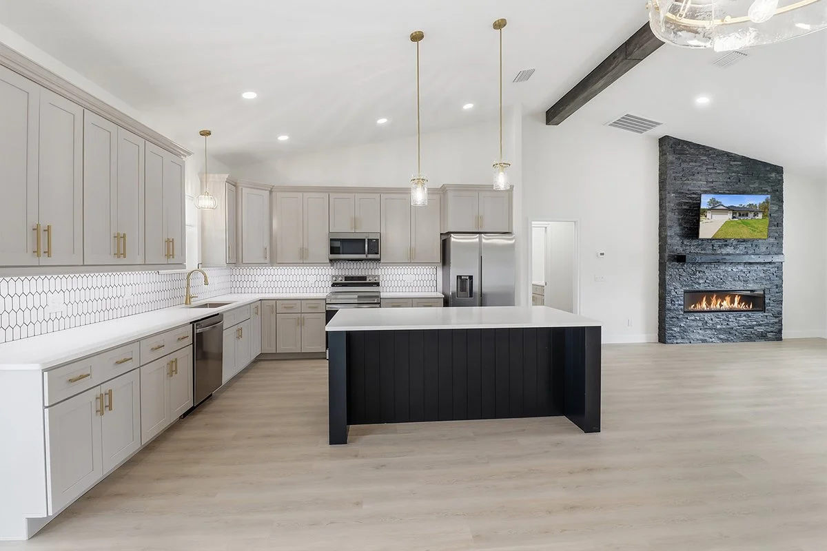 Modern kitchen with light gray cabinetry, gold hardware, stainless steel appliances, and elegant pendant lighting over a large central island.