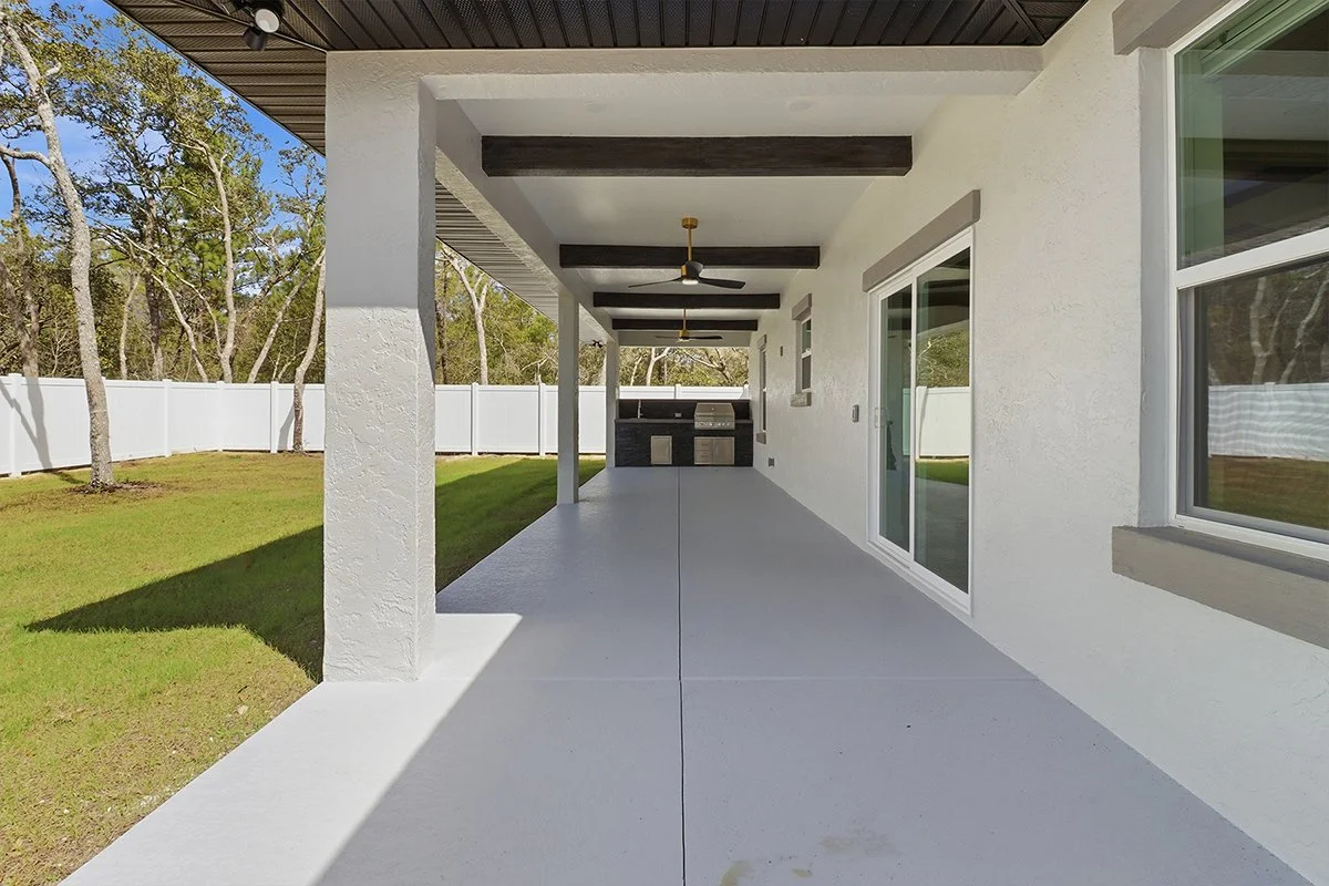 Outdoor living space with a concrete floor, ceiling fans, and a stone-clad outdoor kitchen area with a stainless steel grill.