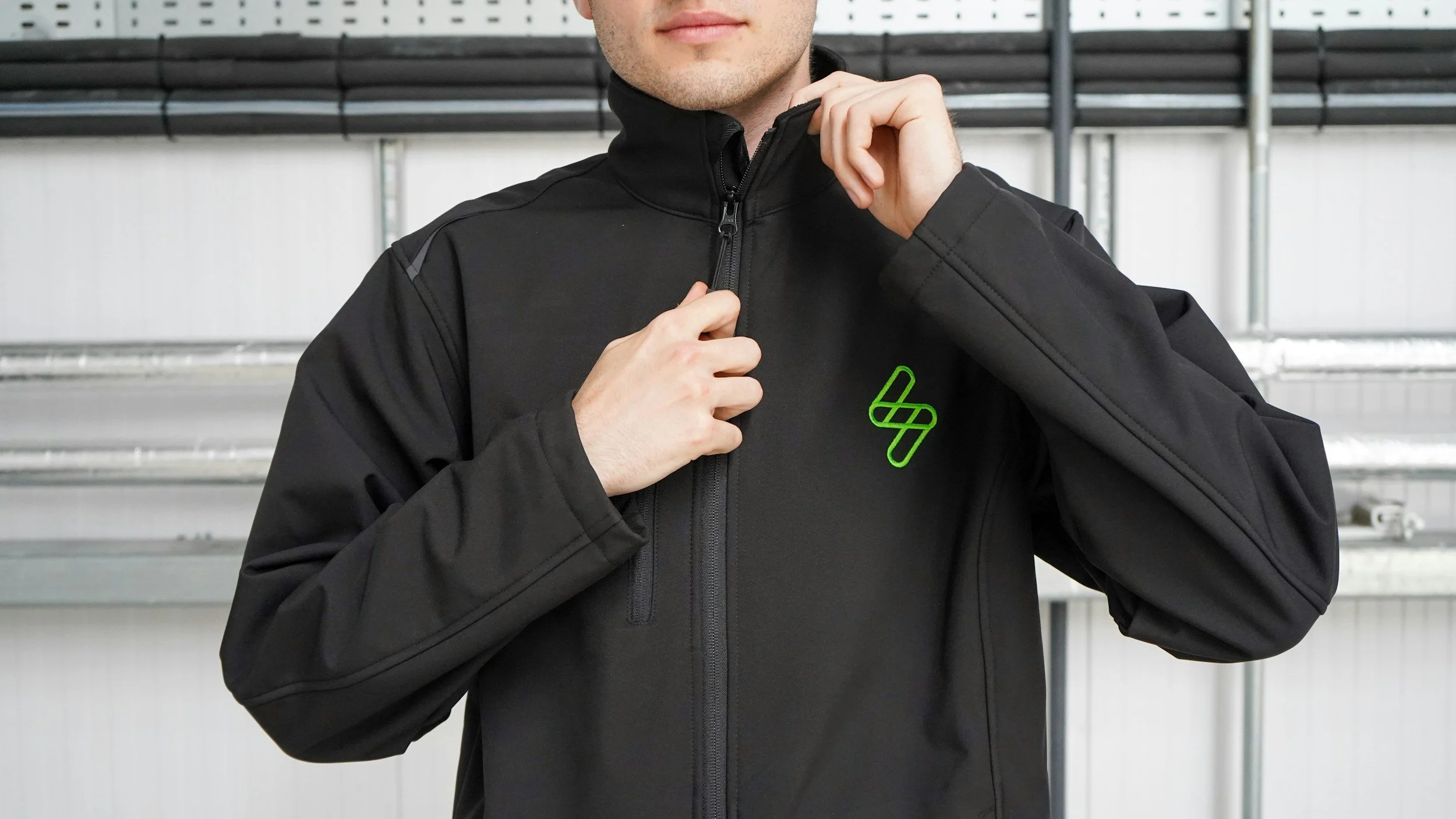 Man zipping a black jacket with a green electricity bolt electrician logo