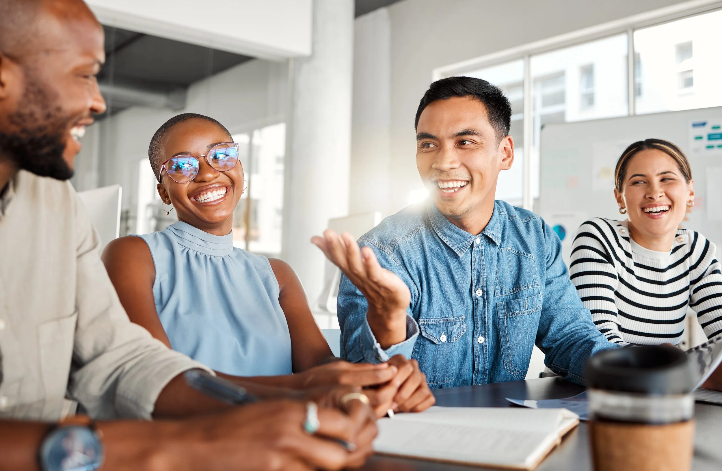 Group of diverse people sitting around a table, engaging in a lively discussion, smiling, and making eye contact in a modern office setting.