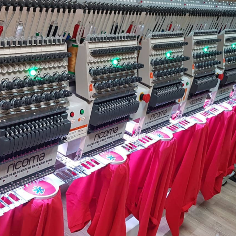 Multiple embroidery machines stitching pink fabric with red fabric hanging from the work area.