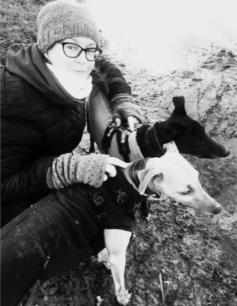Tree, a neurodivergent English teacher is wearing winter clothes and holding two whippets, also wearing winter clothes!