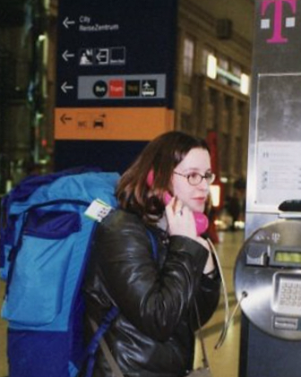 A colour picture taken in 1999. Tree Blackmore has a big blue rucksack on her back and is on the phone in a German train station. The Deutsche Telefon phone is bright pink.