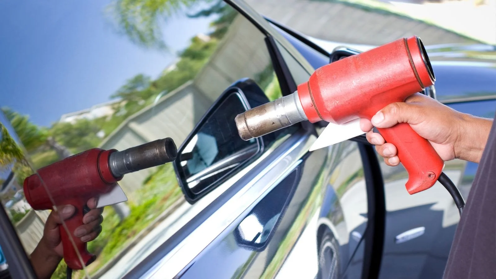 Person repairing a car window using a heat gun from outside the vehicle.