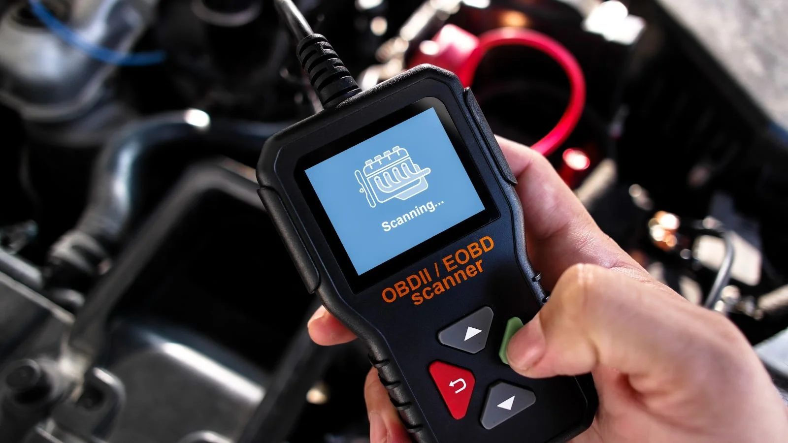 A person holding a portable OBDII/EOBD scanner device, which displays a scanning icon on its screen.